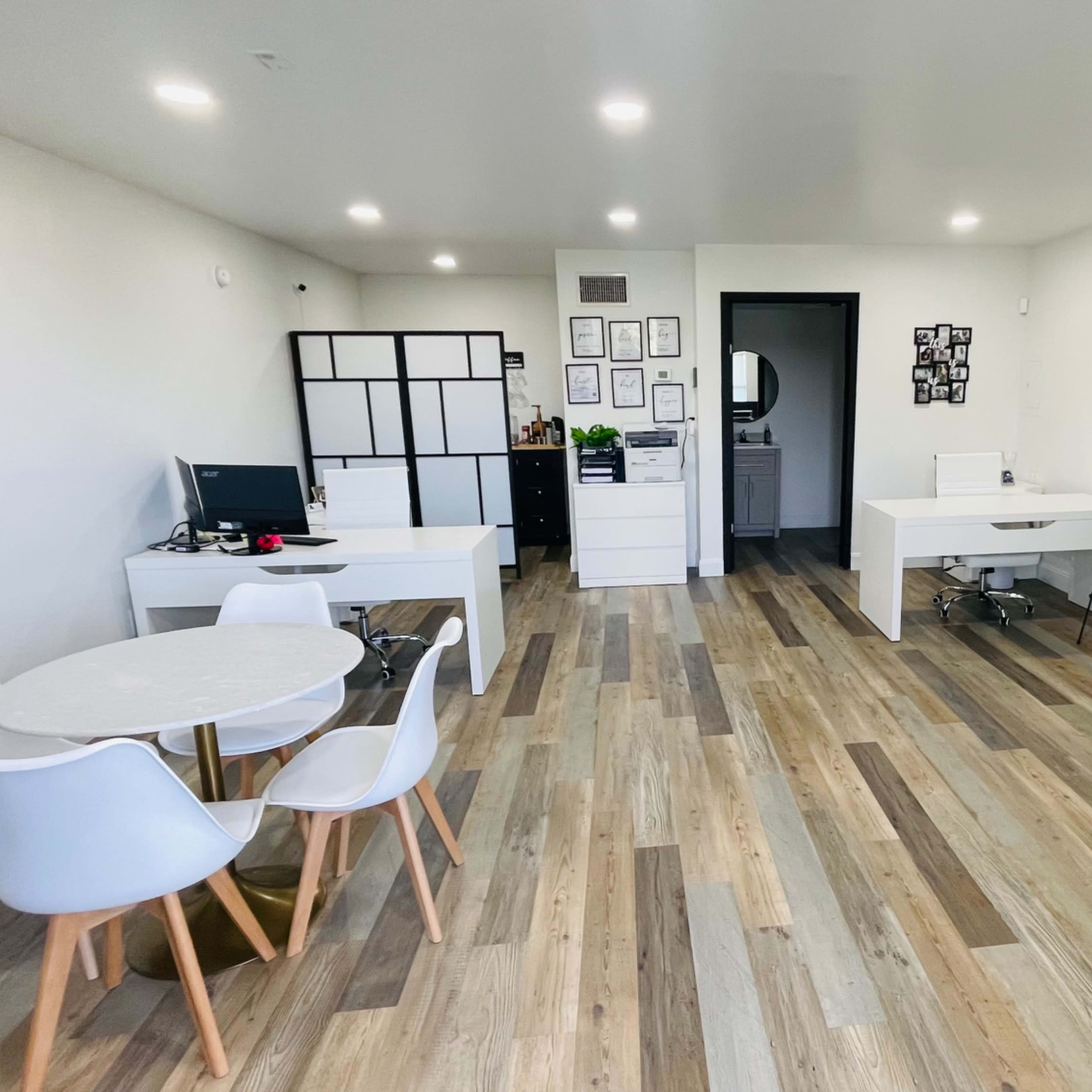 A modern office space with white furniture, wooden flooring, and a green wall feature.