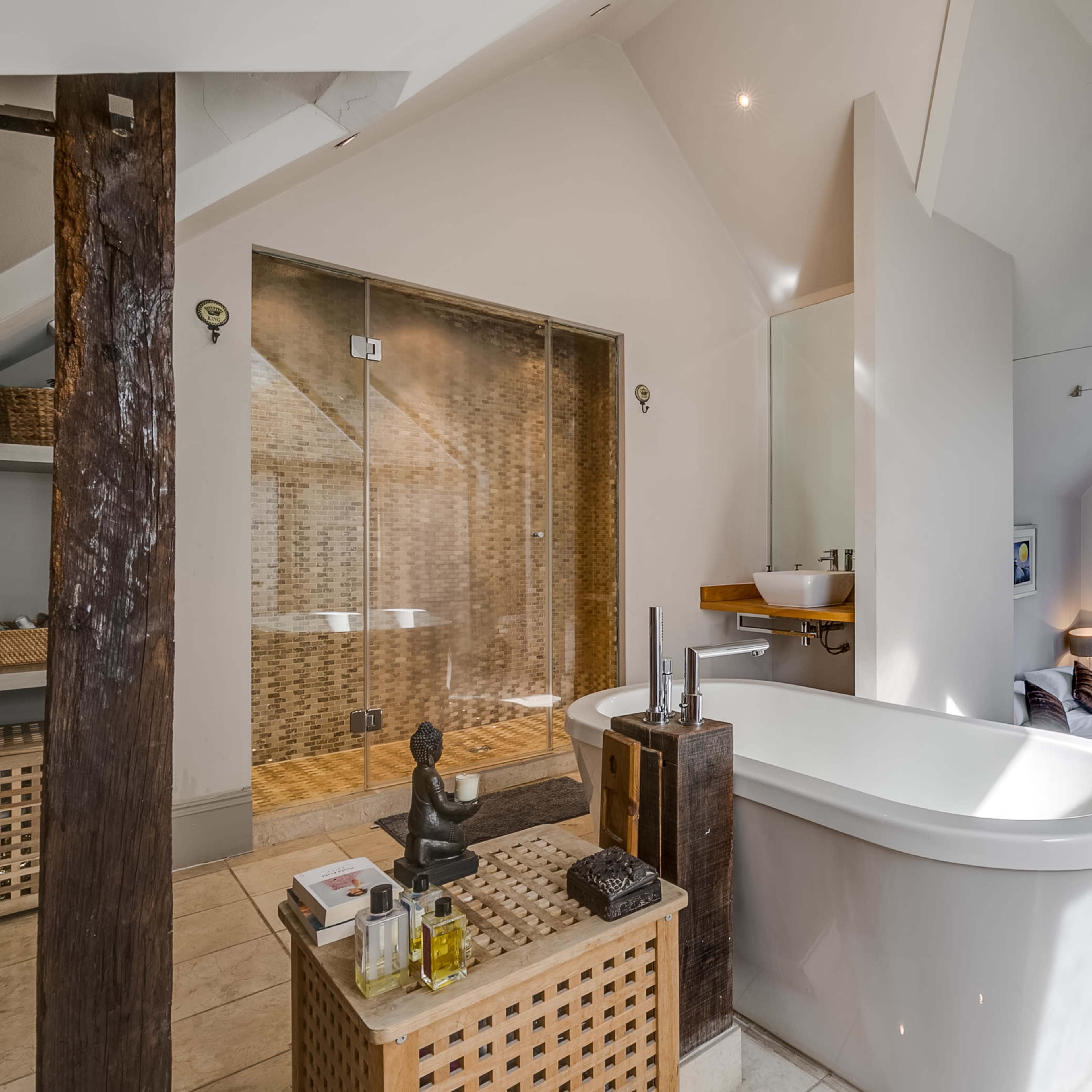 A modern bathroom featuring a freestanding bathtub, a glass shower enclosure, and a toilet, with wooden accents and decorative items on a side table.