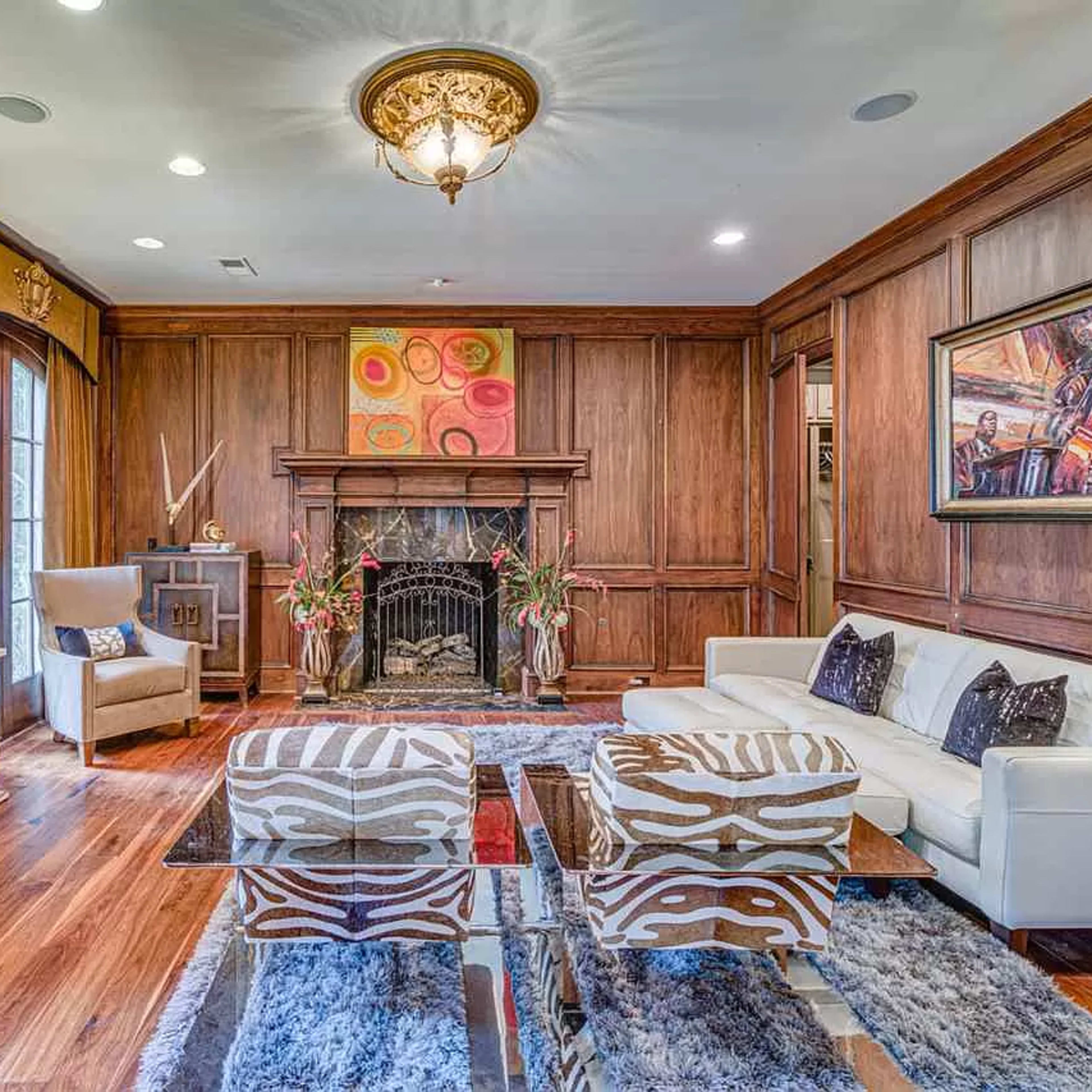 A polished living room with wooden paneling, a fireplace, and a mix of modern and traditional furniture, including a white sofa and zebra-striped chairs.