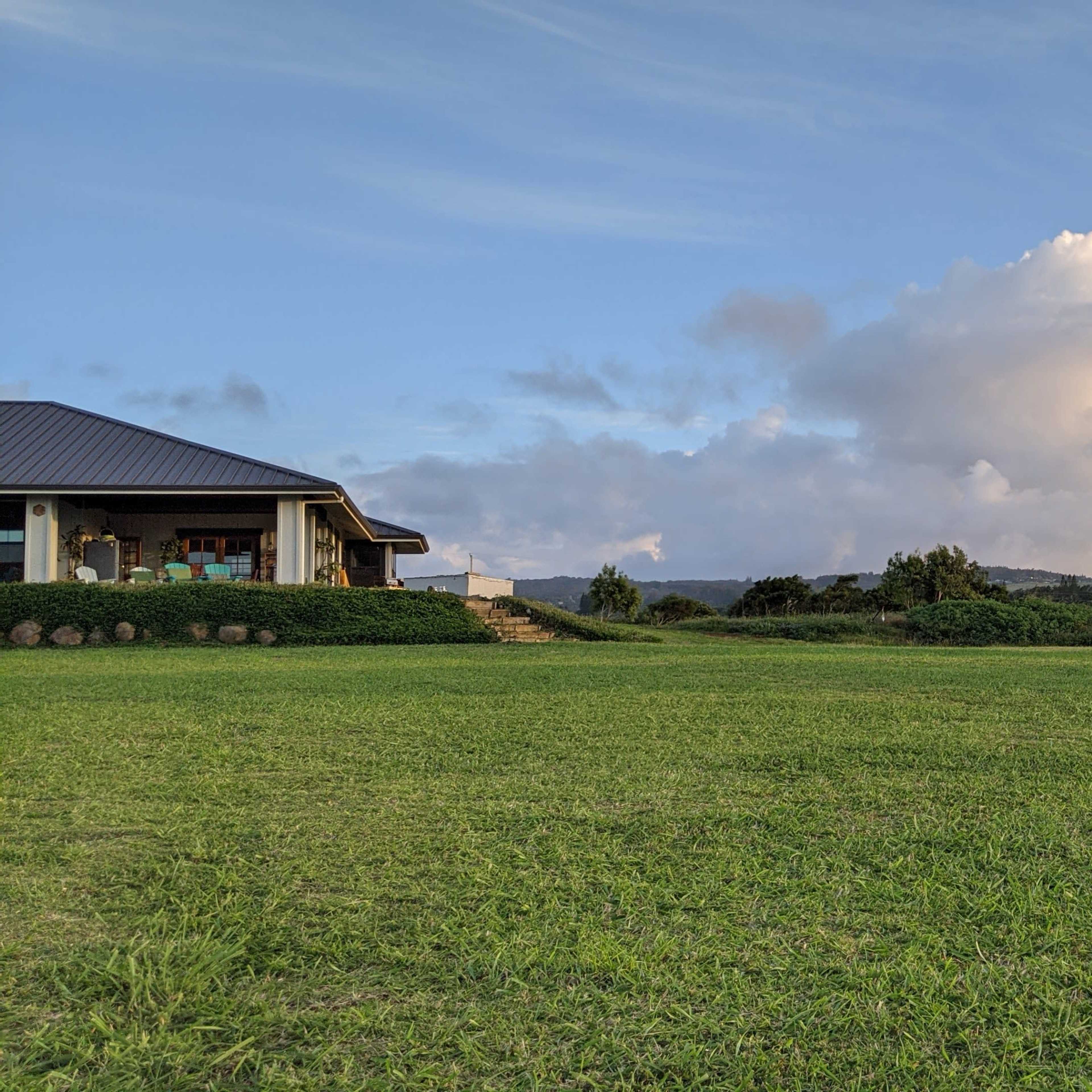 A house with a covered porch sits on a grassy field under a cloudy sky.