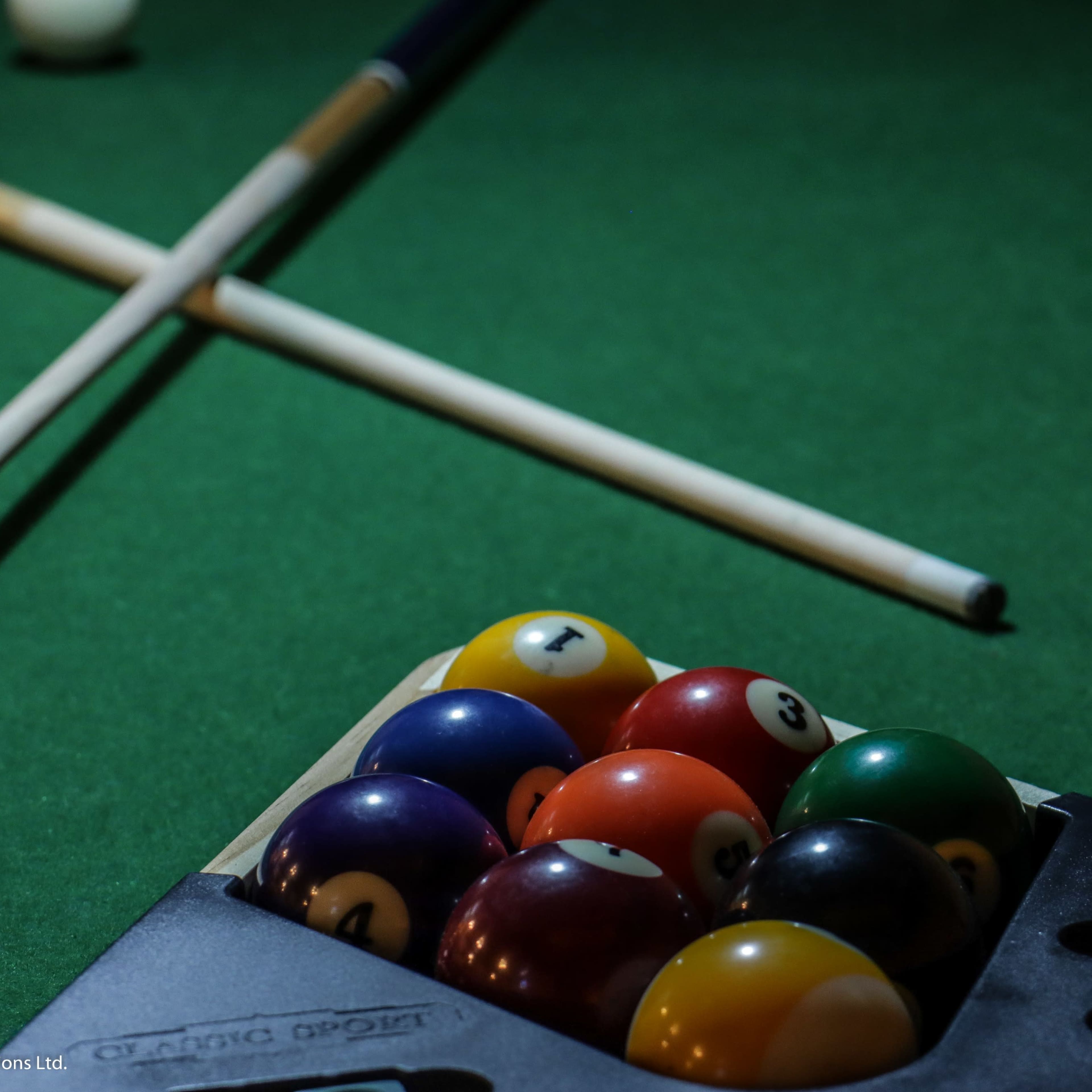 A pool table with a rack of balls and two cue sticks laid across the green felt.