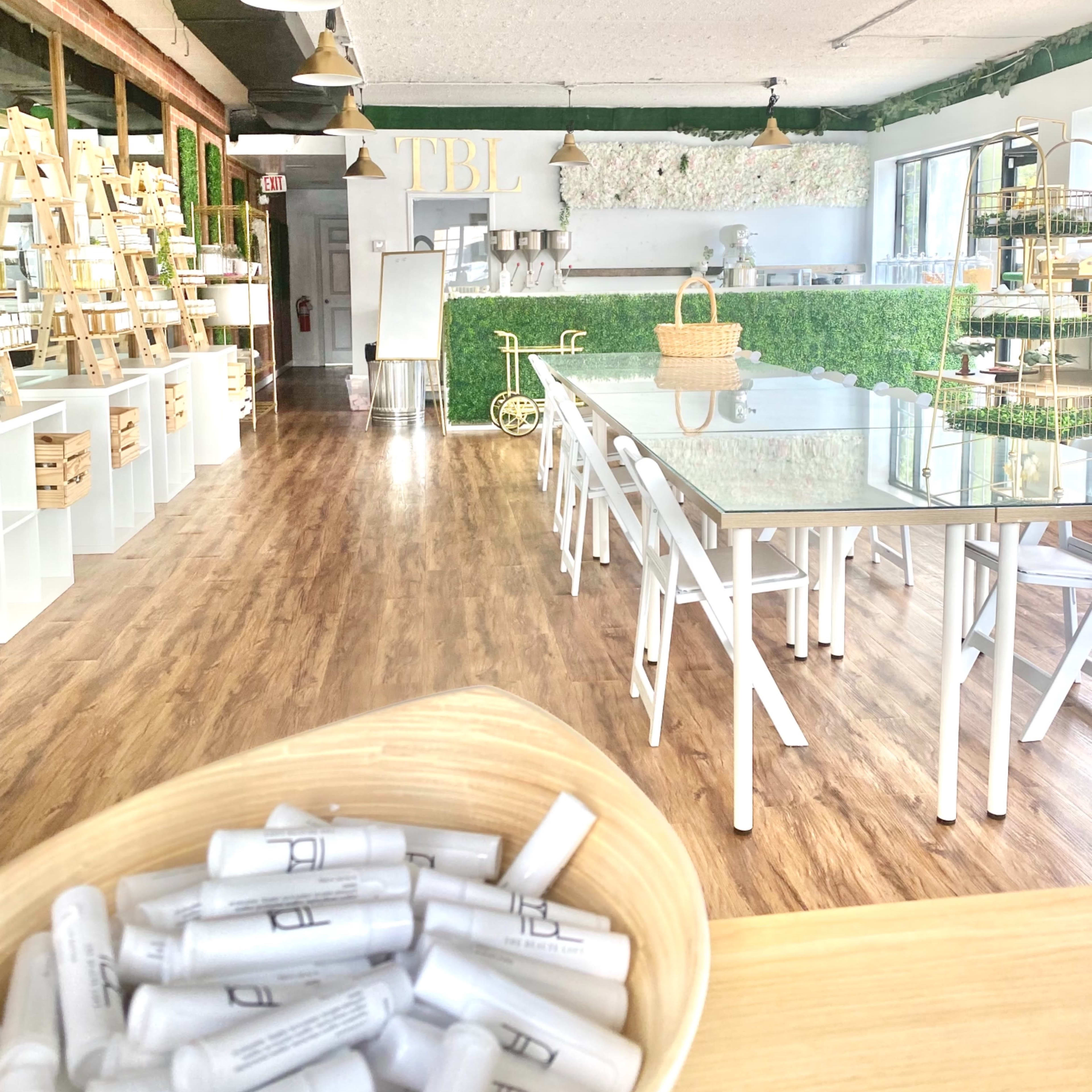 A bright, modern space featuring a wooden floor, white tables, shelves lined with products, and green accents.