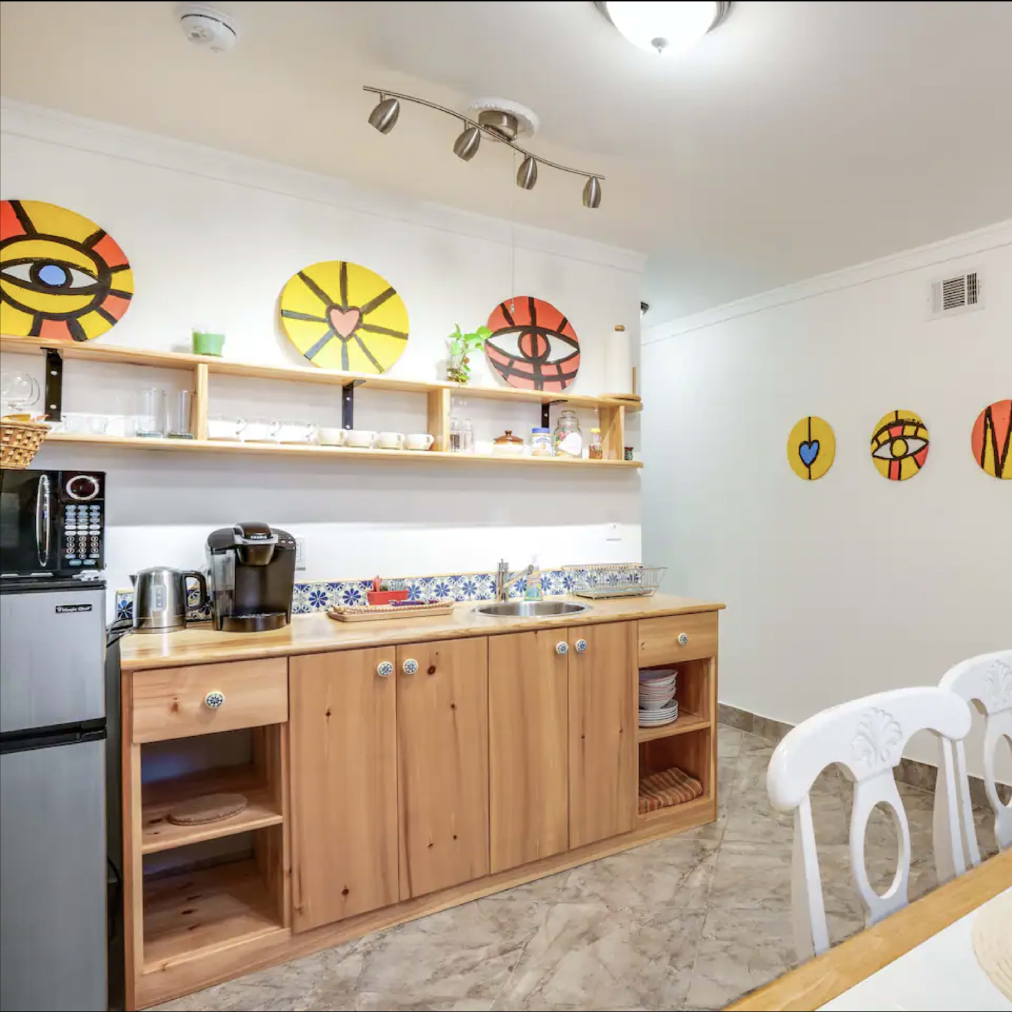 A kitchen with wooden cabinets and shelves, decorated with colorful circular art pieces on the walls.