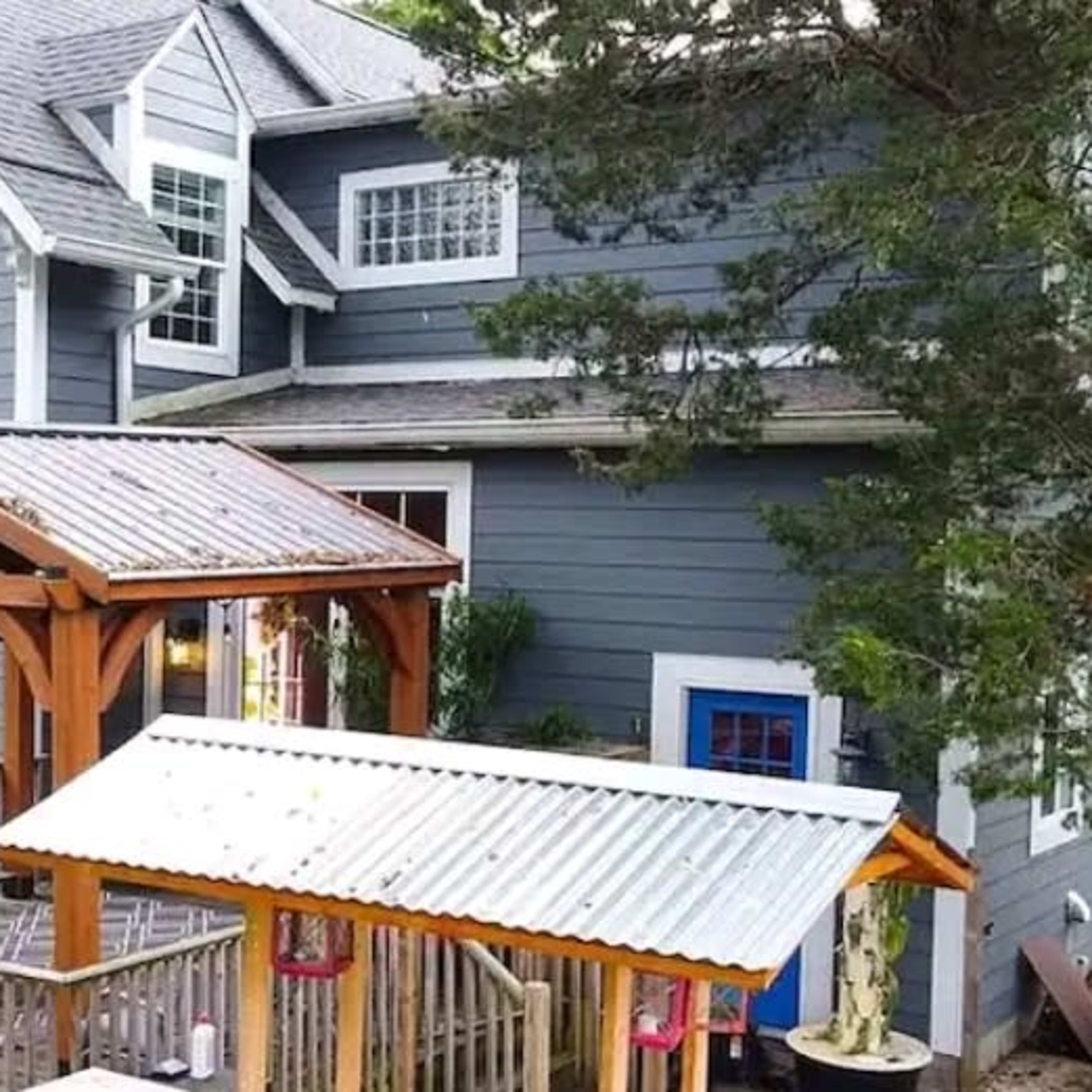 A two-story gray house with multiple windows, a brick chimney, and a wooden deck featuring a gazebo.