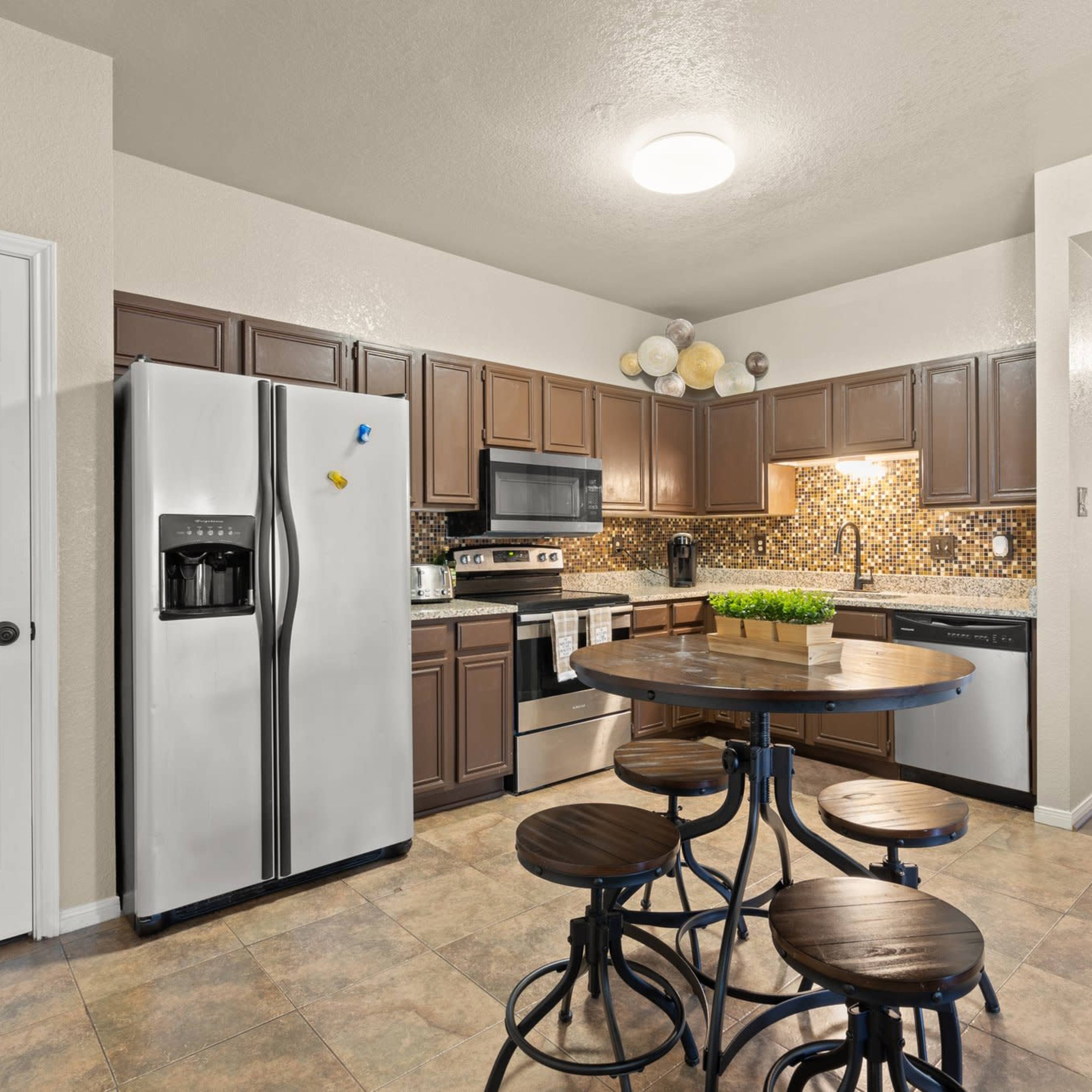 A modern kitchen features stainless steel appliances, dark wooden cabinets, and a round table with metal stools.