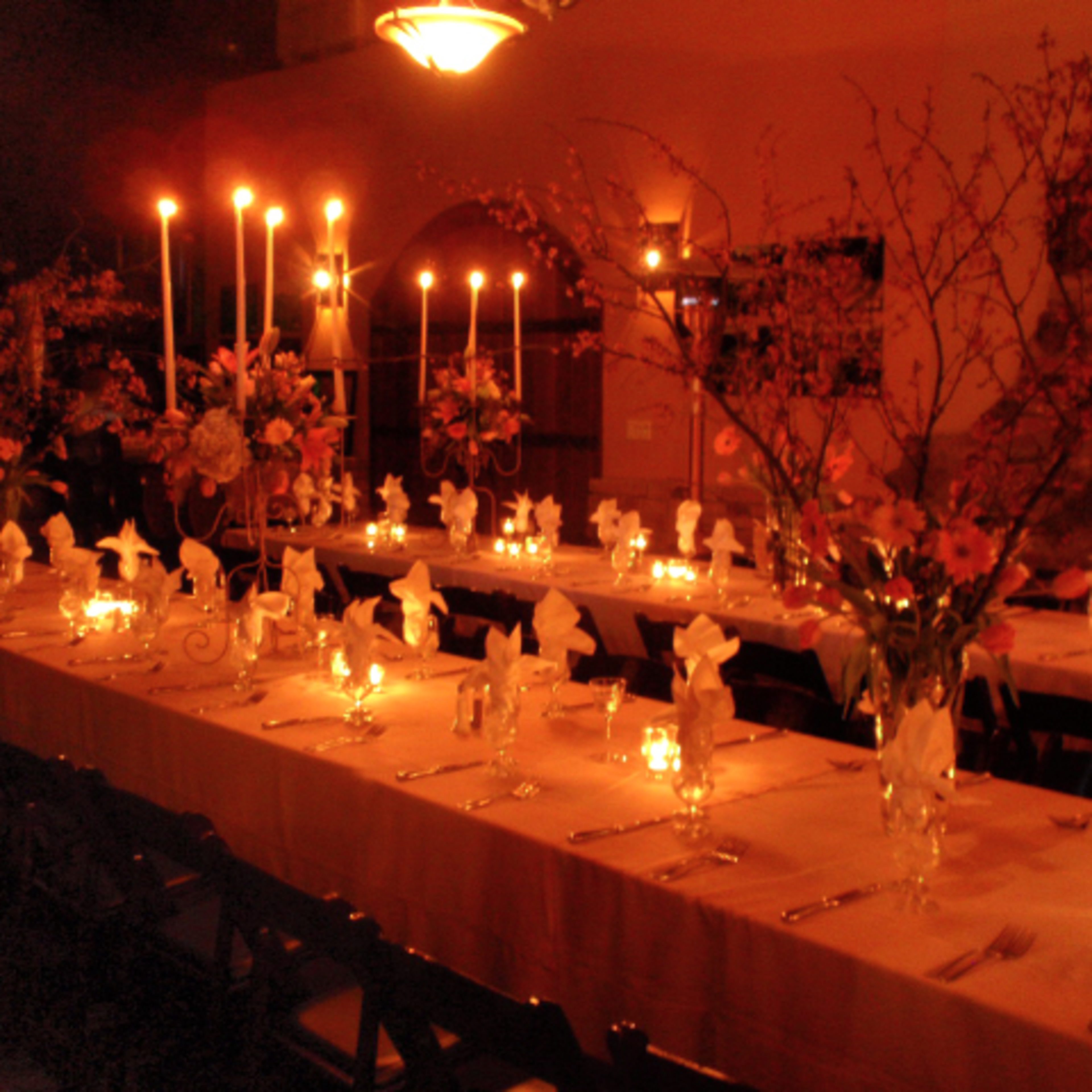 A long table is set for dinner, adorned with flowers, candles, and neatly folded napkins in a dimly lit room.