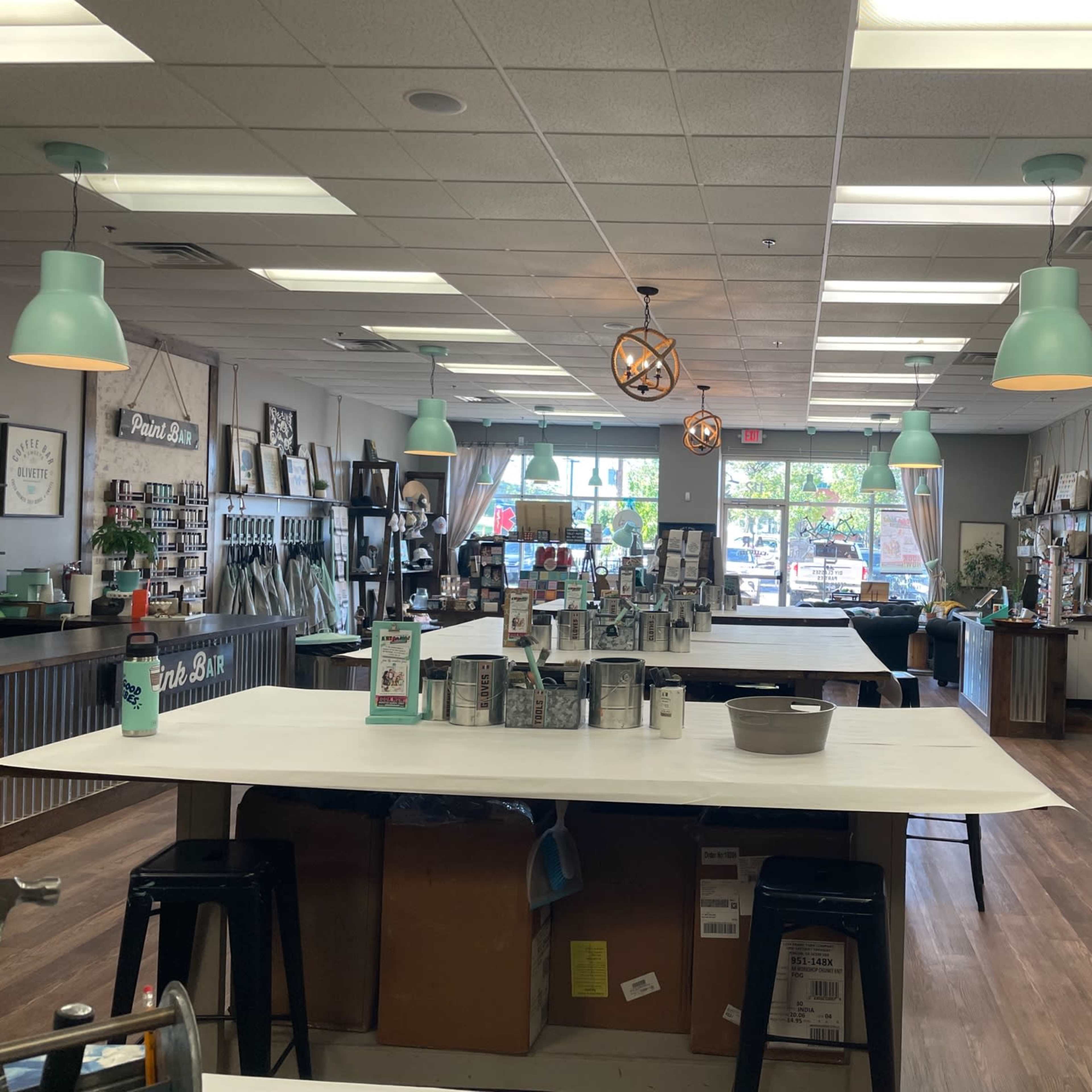 A spacious, well-lit craft studio with tables, various supplies, and decorative wall art, featuring large windows that allow natural light to enter.