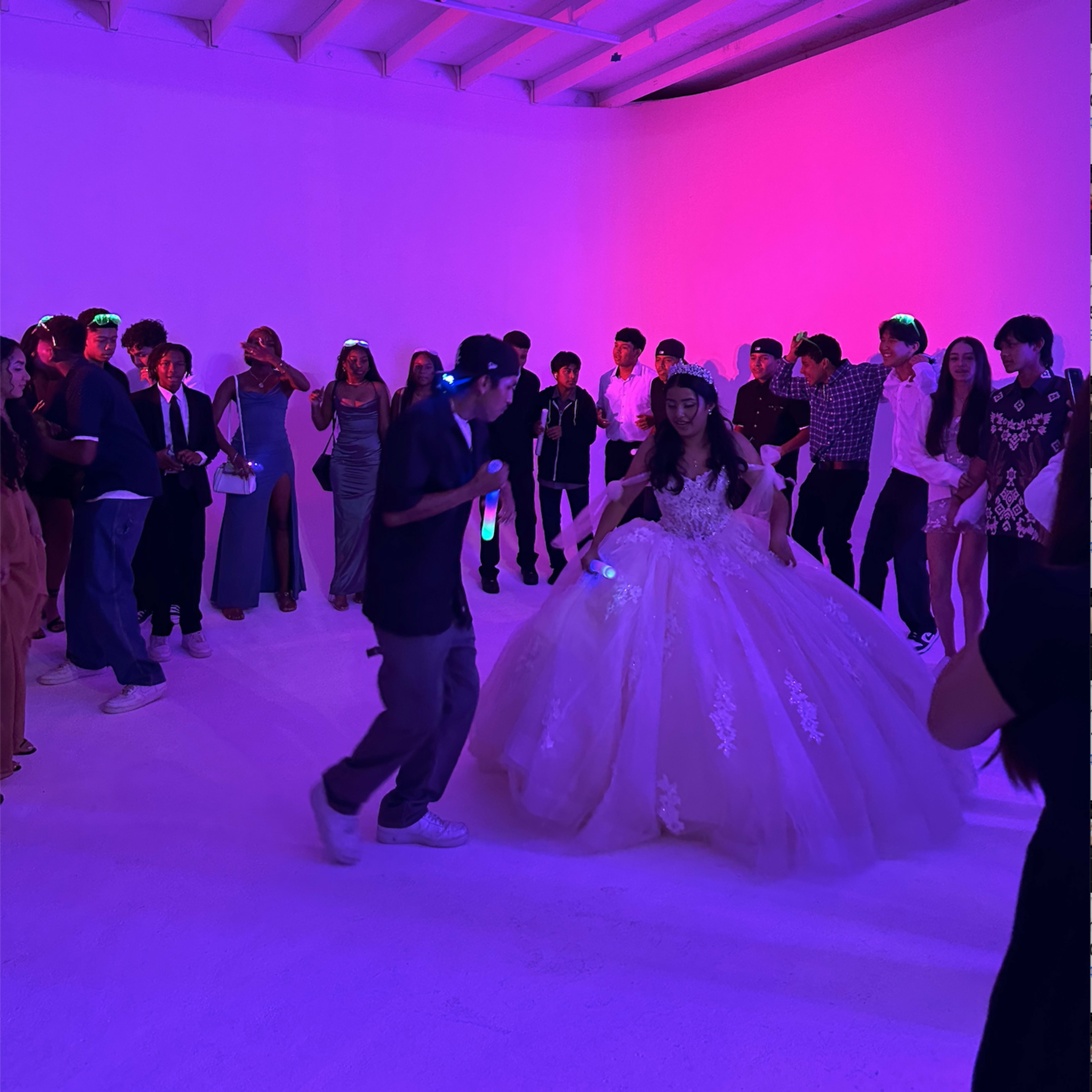 A group of people celebrate in a brightly lit room with a bride in a large white gown dancing among them.