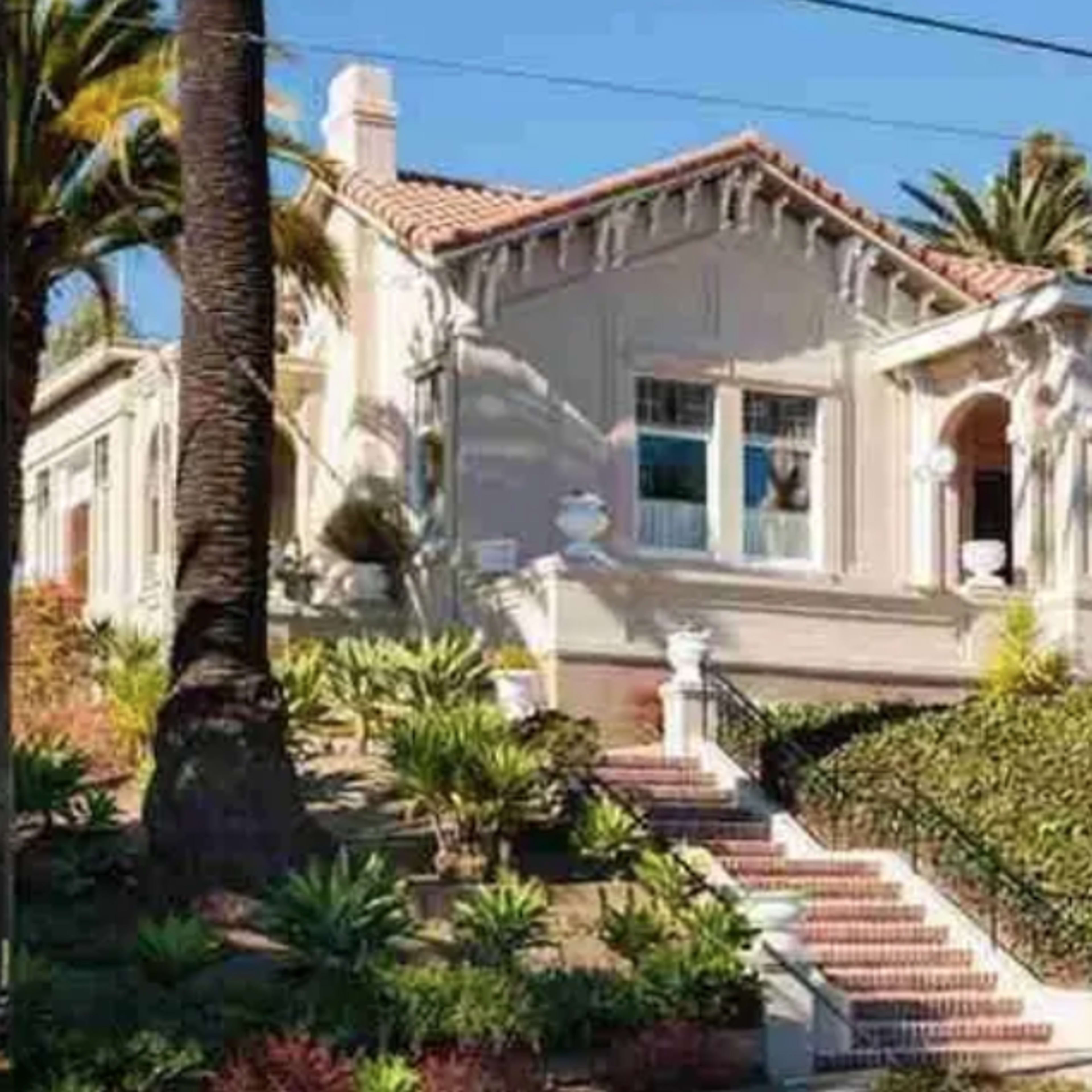 A large, single-story house with a tiled roof is surrounded by palm trees and landscaped gardens.