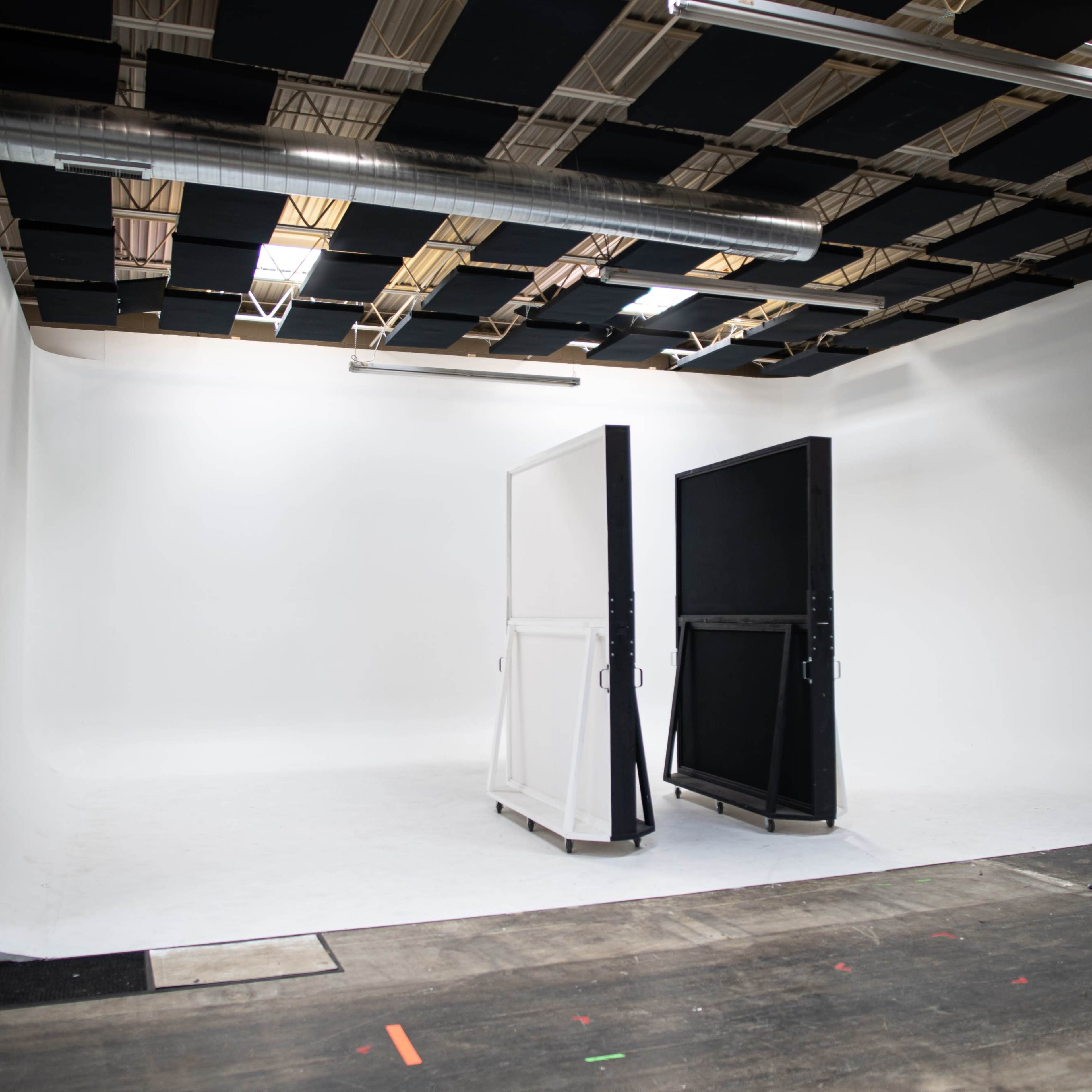 A studio space with a seamless white backdrop, two large panels on wheels, and overhead lighting fixtures.