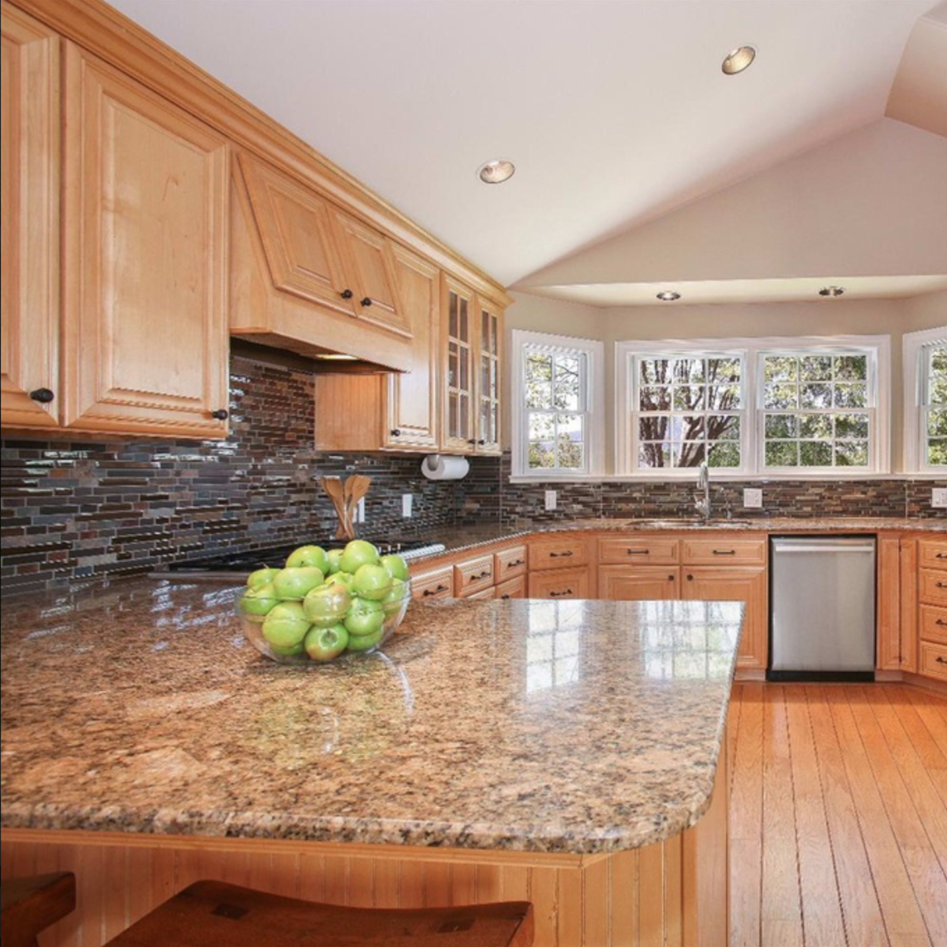 A kitchen features wooden cabinets, a granite countertop with a bowl of green apples, and stainless steel appliances under a sloped ceiling.