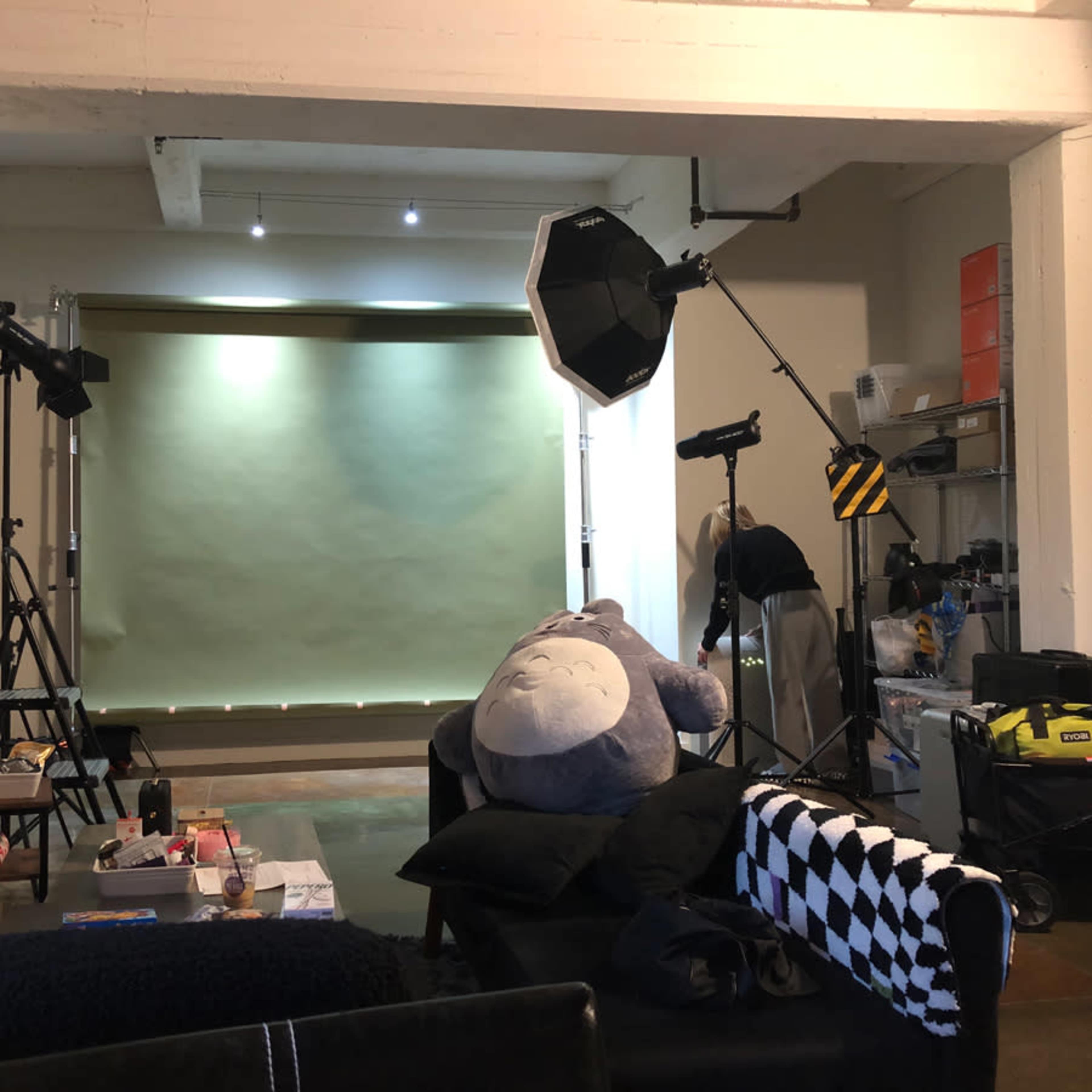 A photography studio is set up with a green backdrop, lighting equipment, and various props scattered around a seating area.