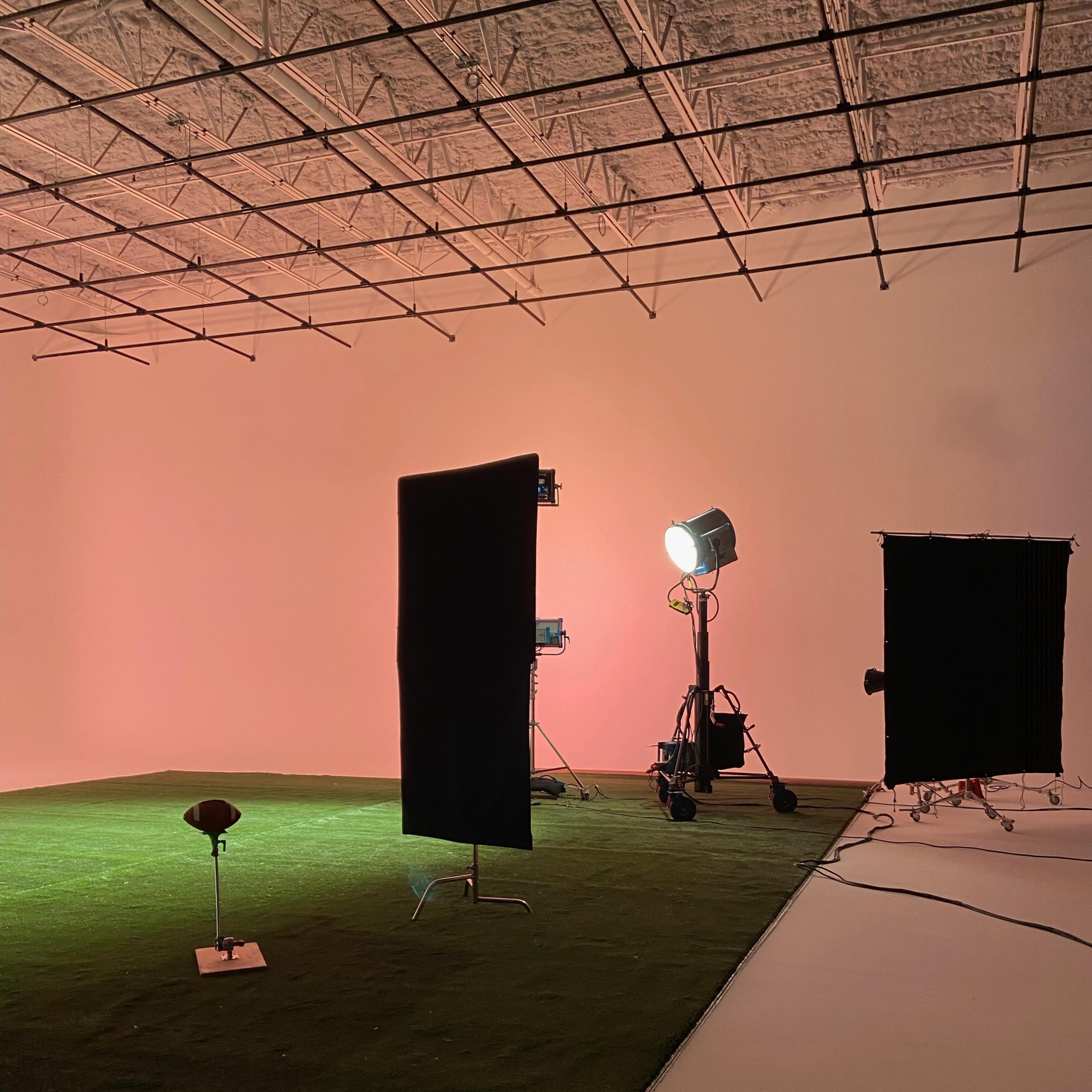 A studio with green artificial grass flooring, black backdrops, and lighting equipment set up for a photo shoot.