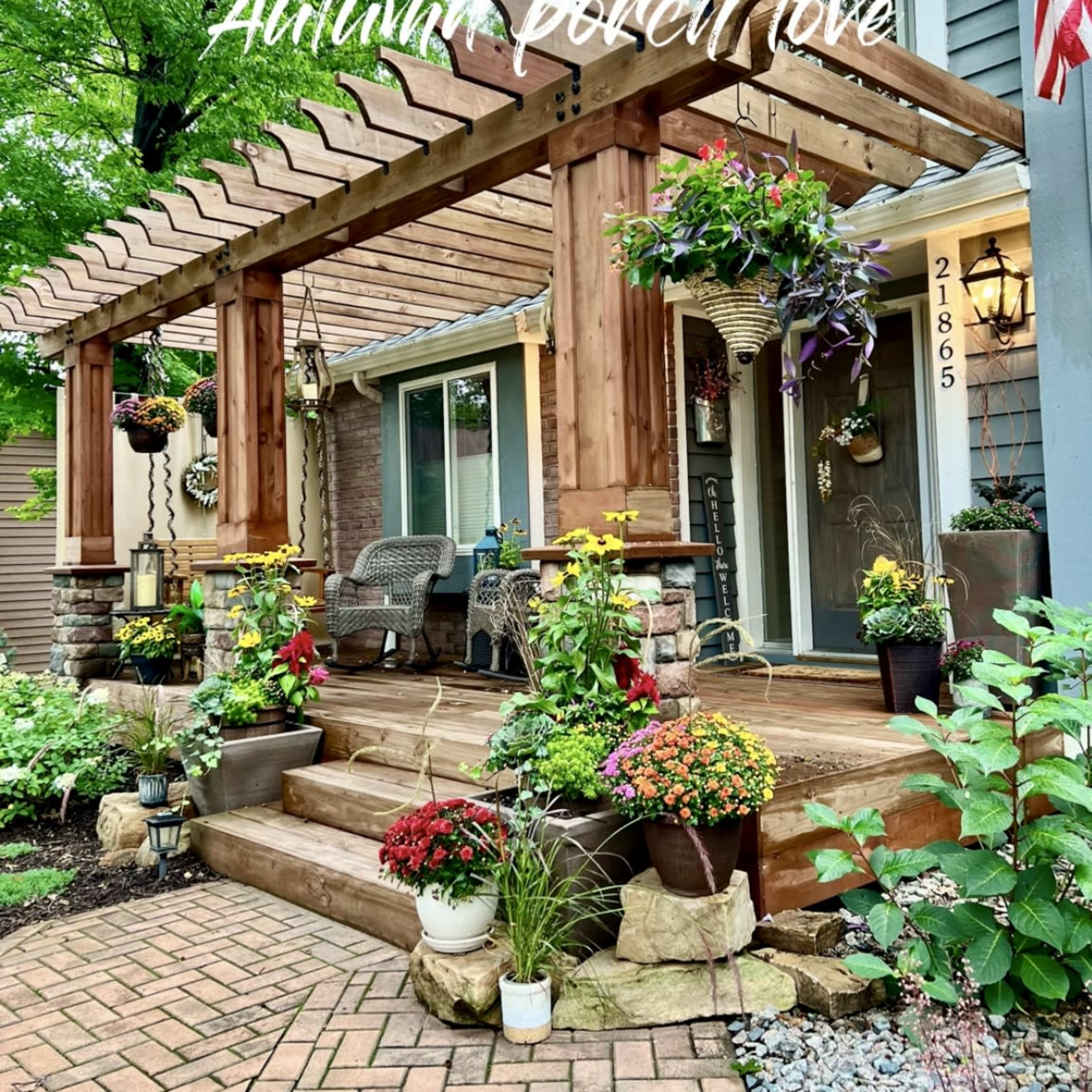 A front porch with a wooden pergola adorned with hanging flower pots and a variety of potted plants arranged on the steps and walkway.