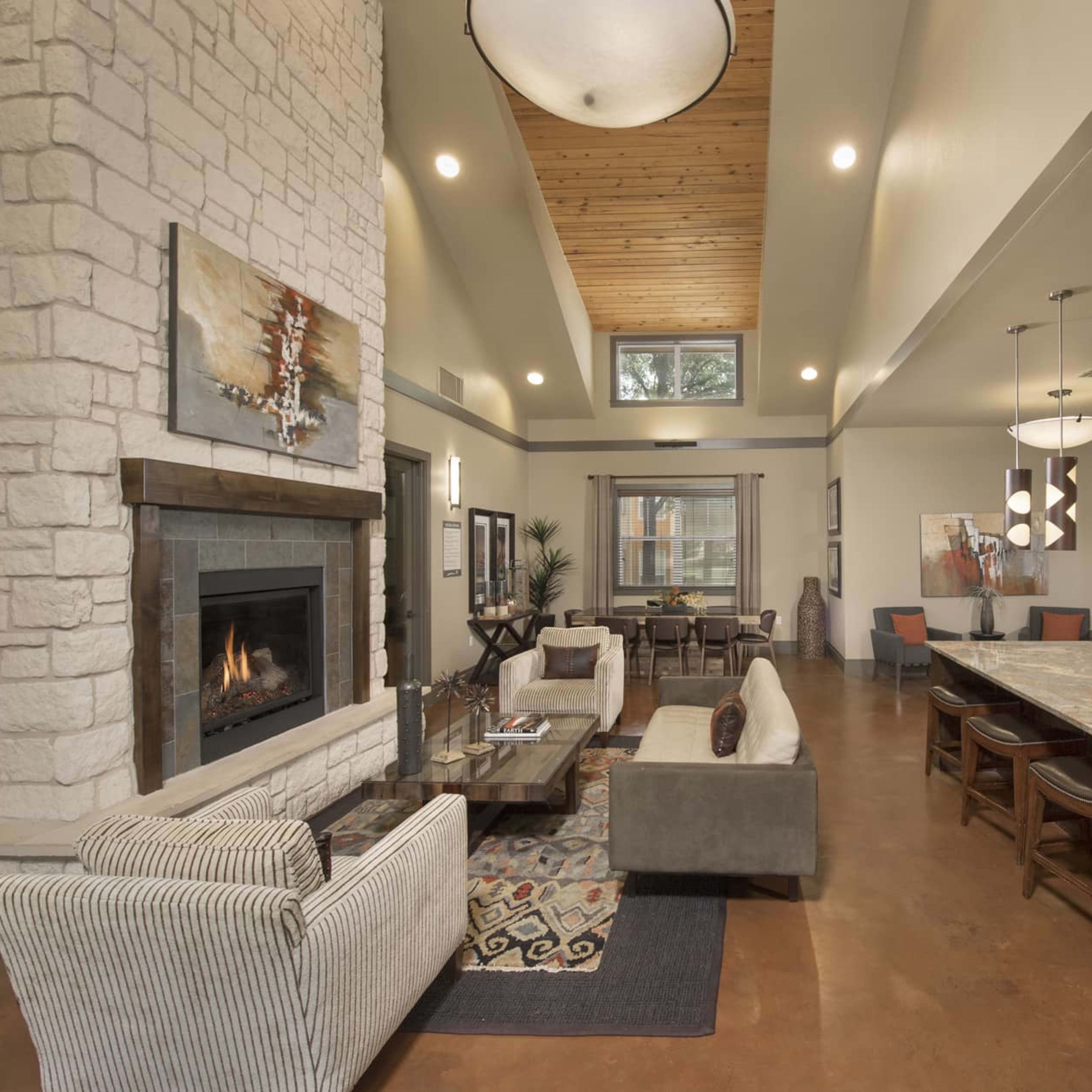 A modern living space features a stone fireplace, a large kitchen island with seating, and a mix of cozy furniture arranged around the room.