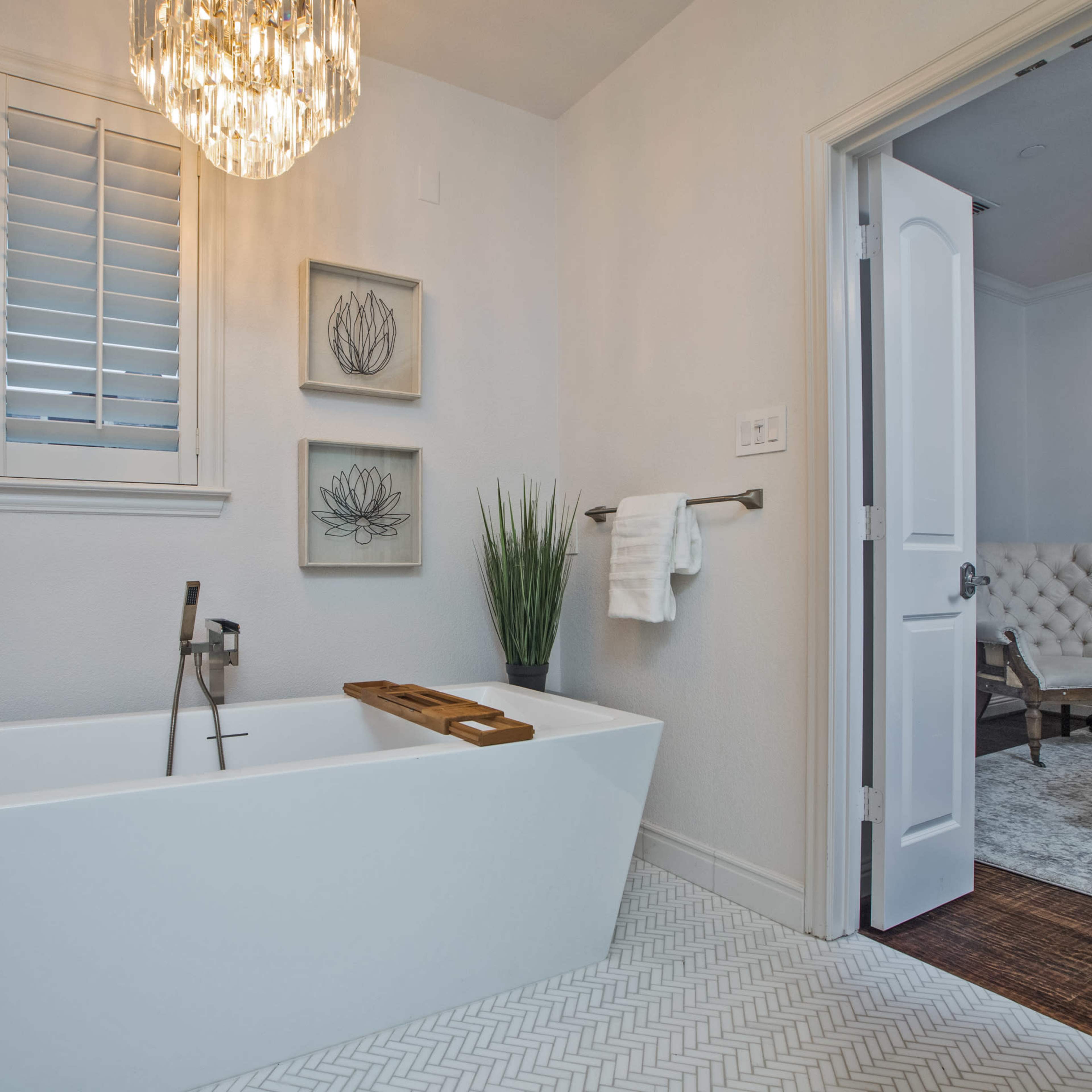 A modern bathroom featuring a freestanding soaking tub, a large light fixture, and a doorway leading to a bedroom.