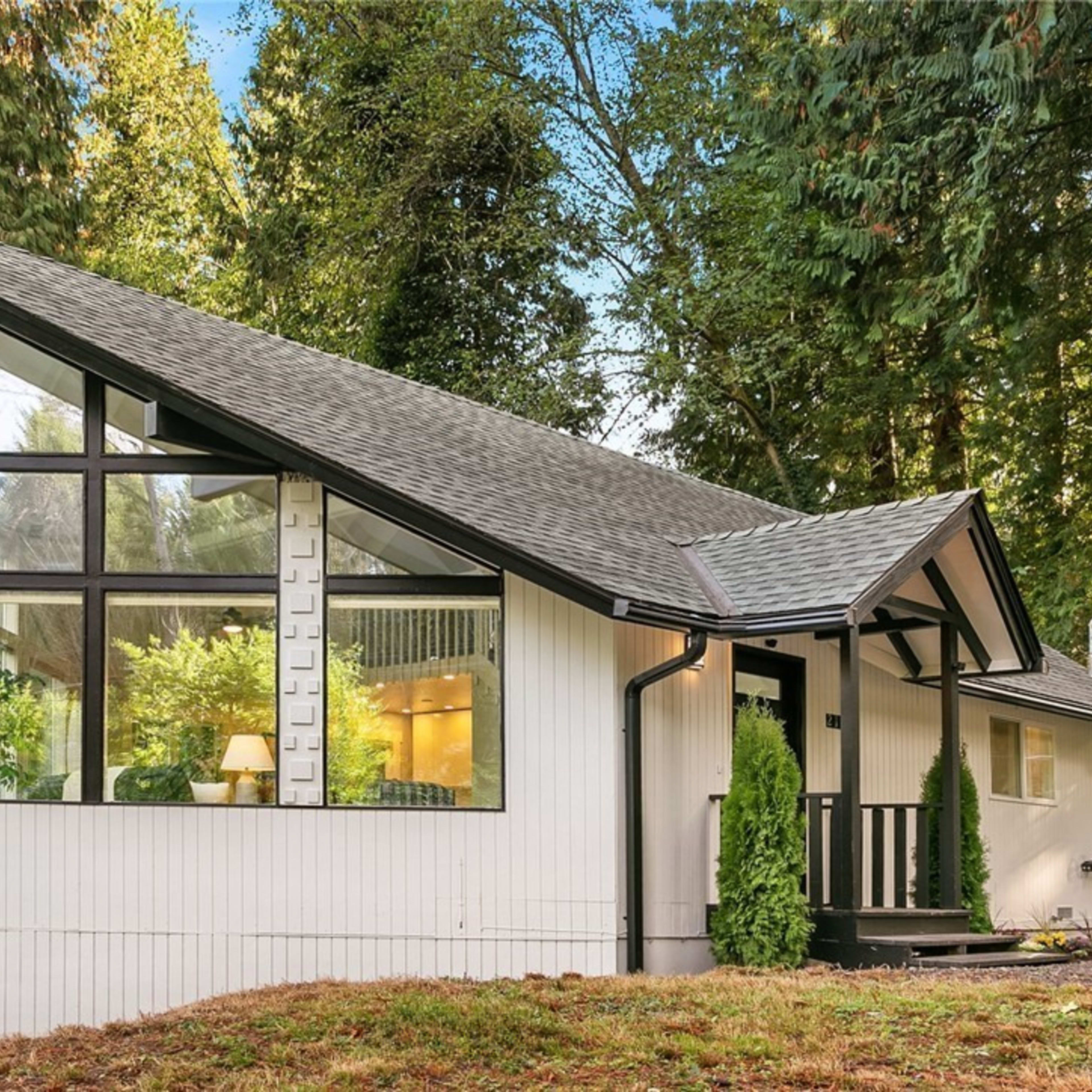 A modern house with a distinctive angular roof and large windows, set among tall trees in a forested area.