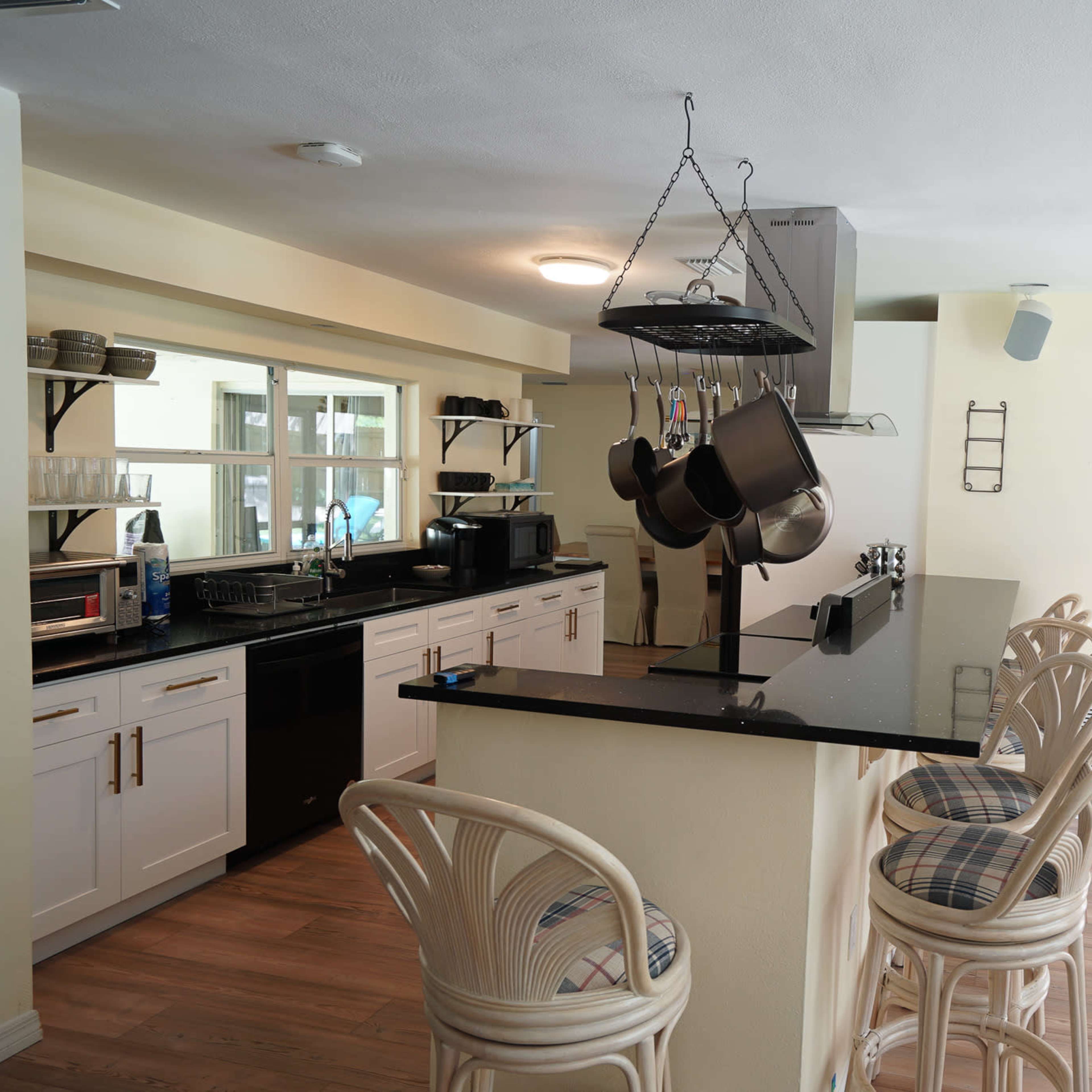 A modern kitchen with a bar-style countertop, equipped with hanging pots and a bright entrance door.