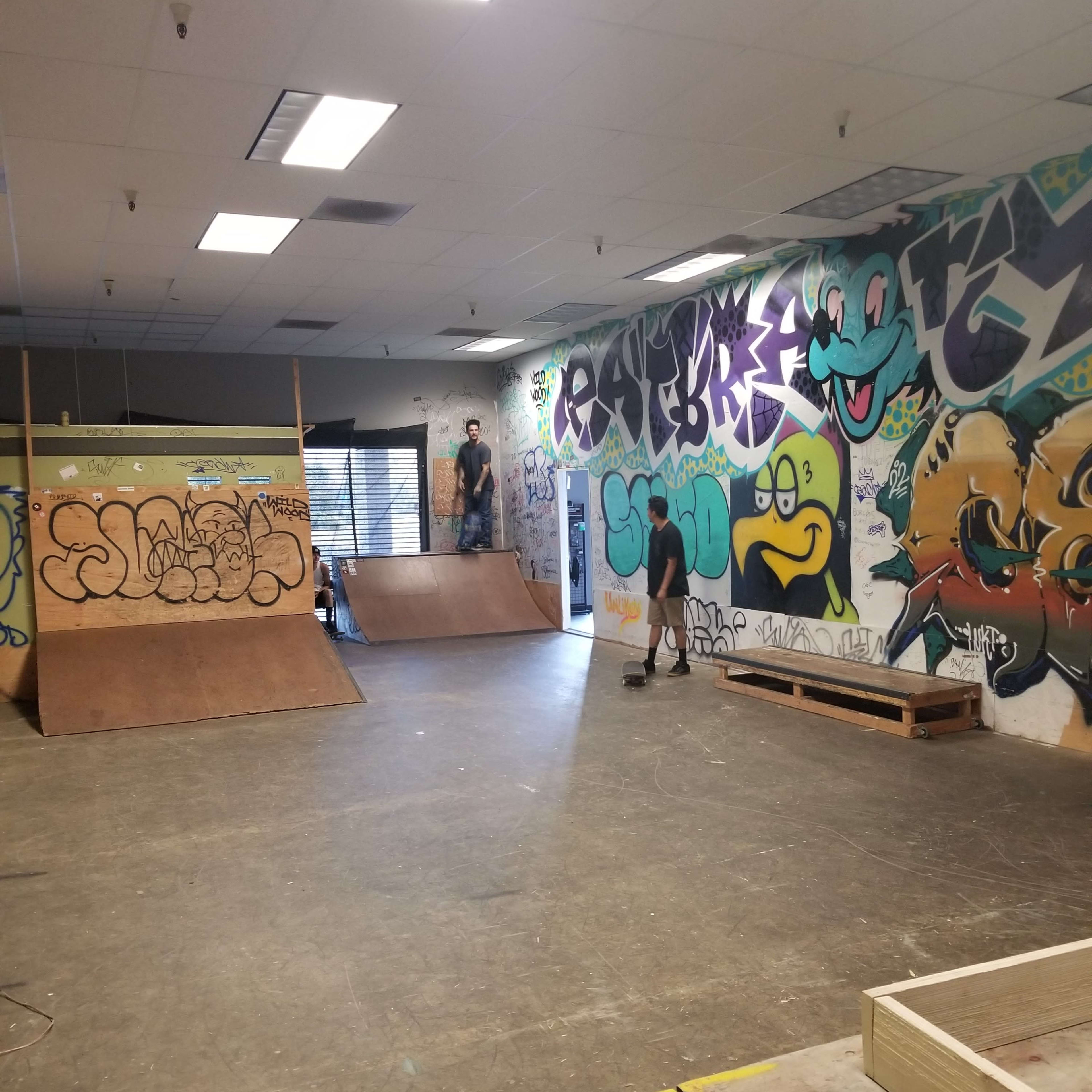 An indoor skate park with wooden ramps and colorful graffiti-covered walls.