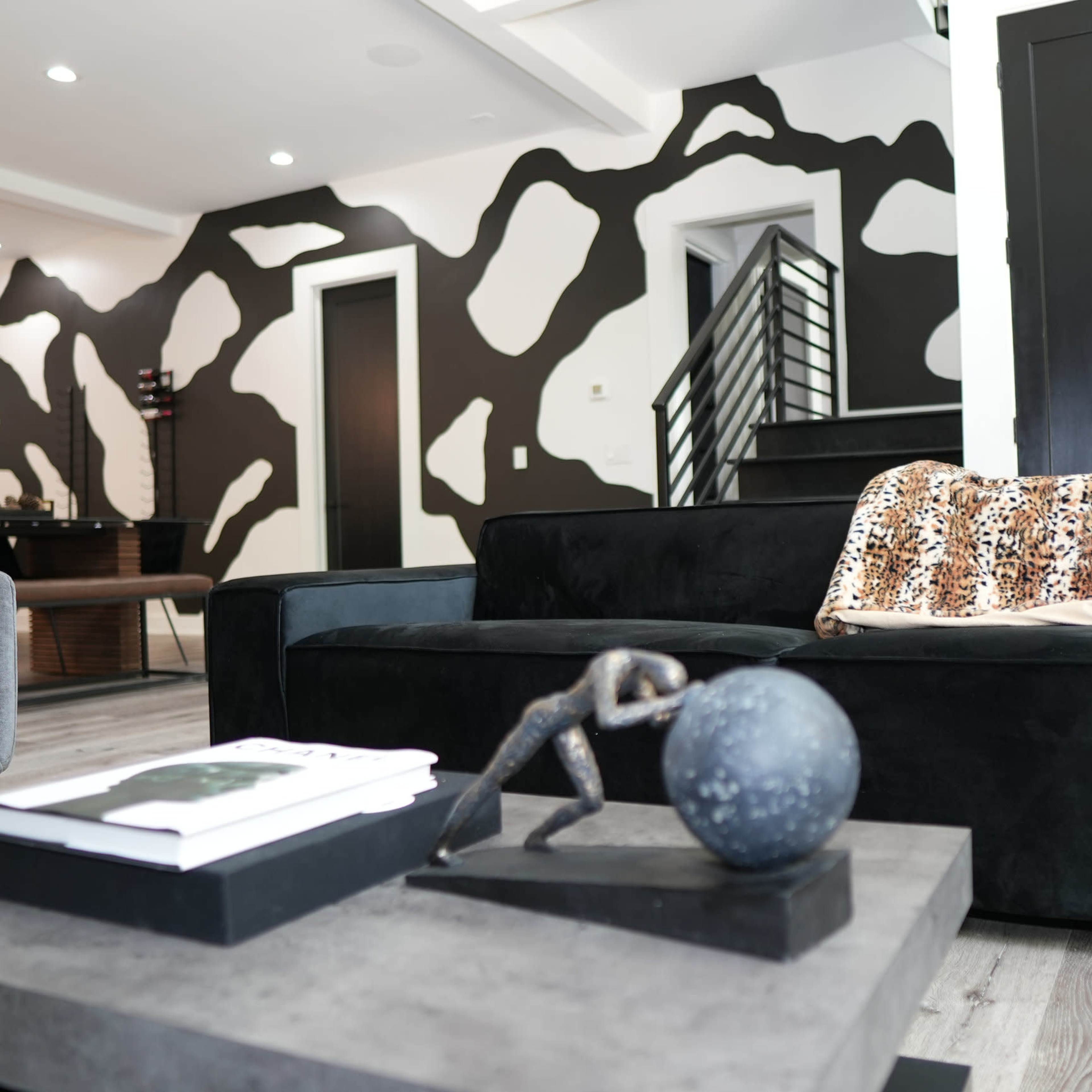 A modern living room with a black couch, a decorative coffee table featuring a sculpture, and a wall adorned with an abstract black and white pattern.