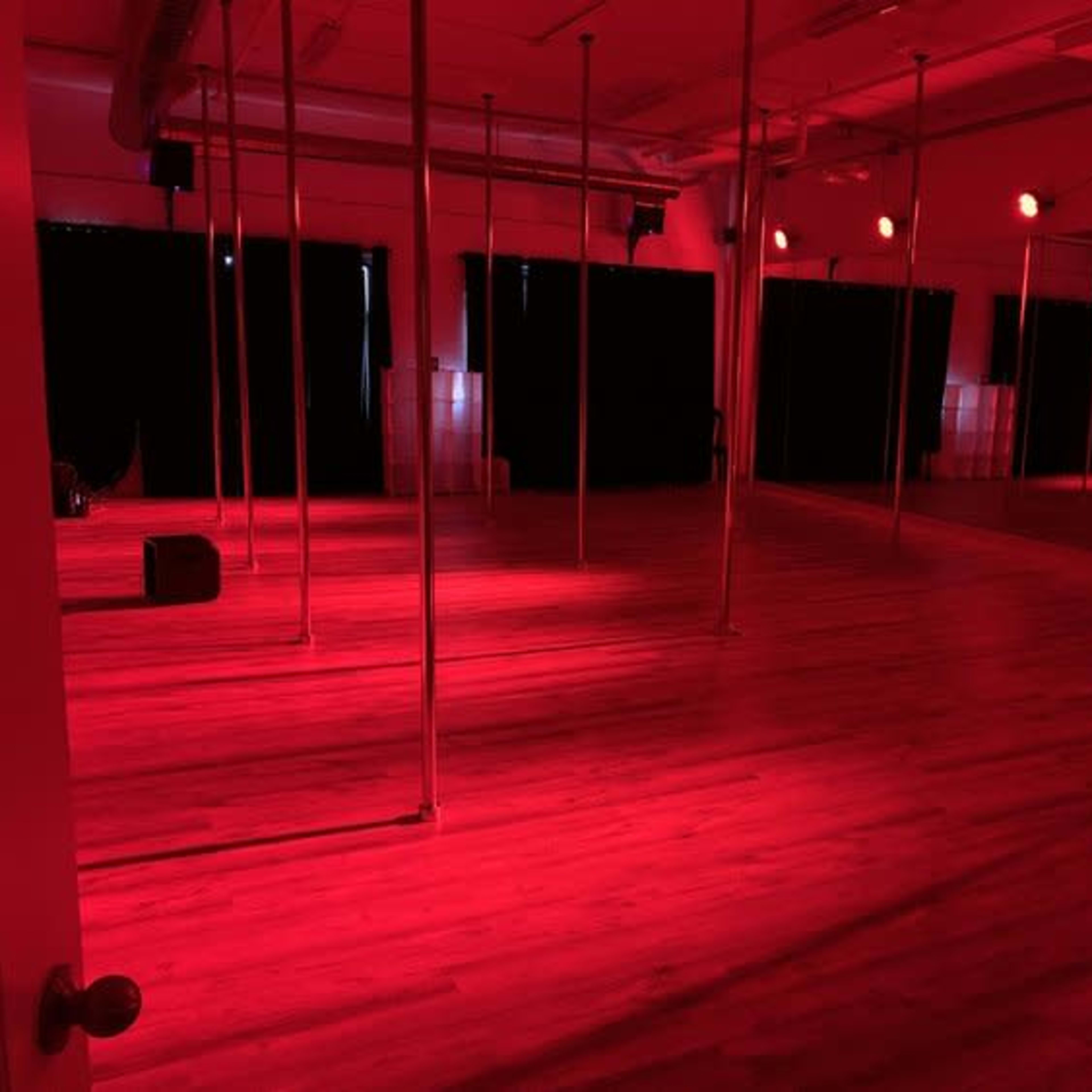 A studio with polished wooden floors and several vertical poles is lit by red ambient lighting.