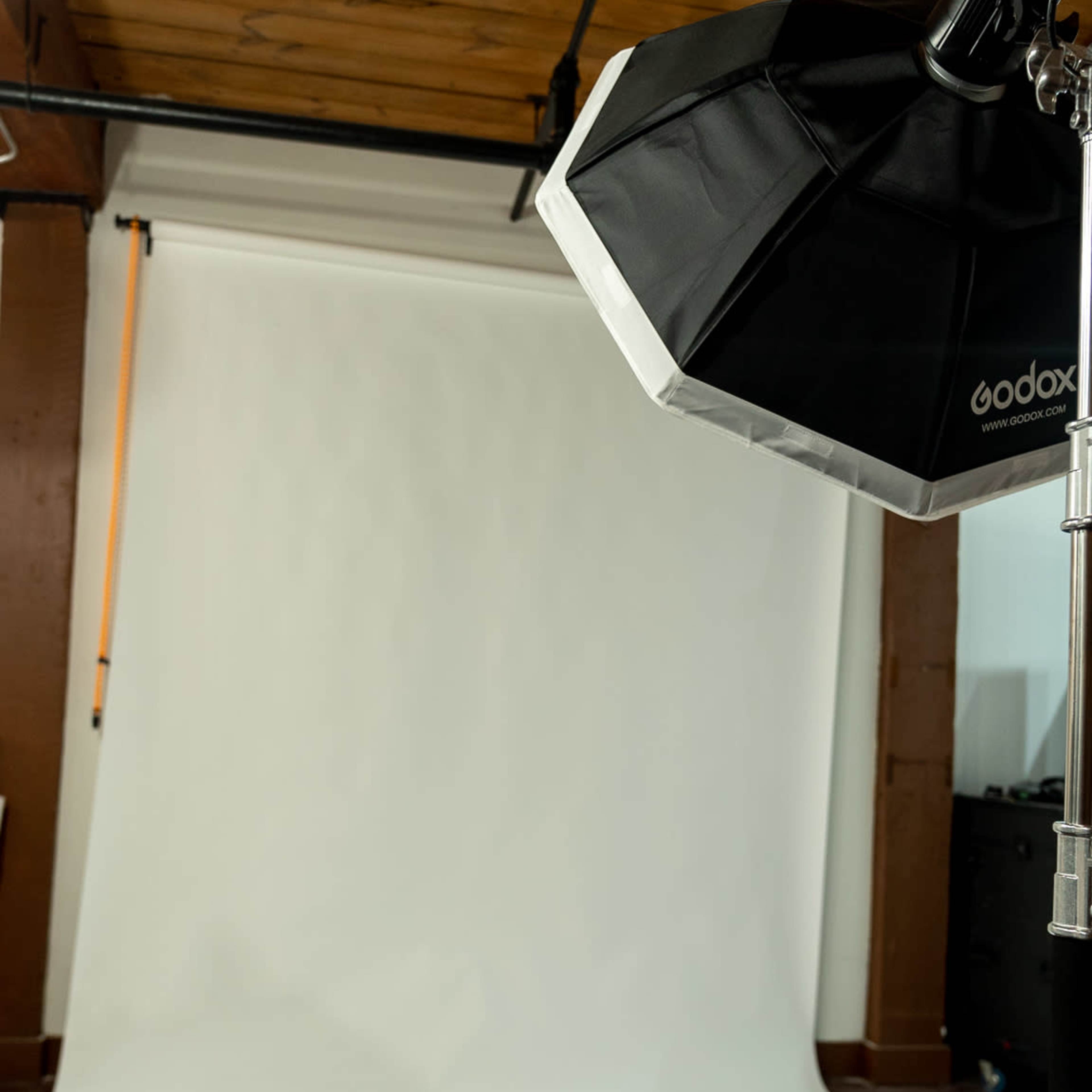 A photography studio is set up with a white backdrop and a softbox light on a stand.