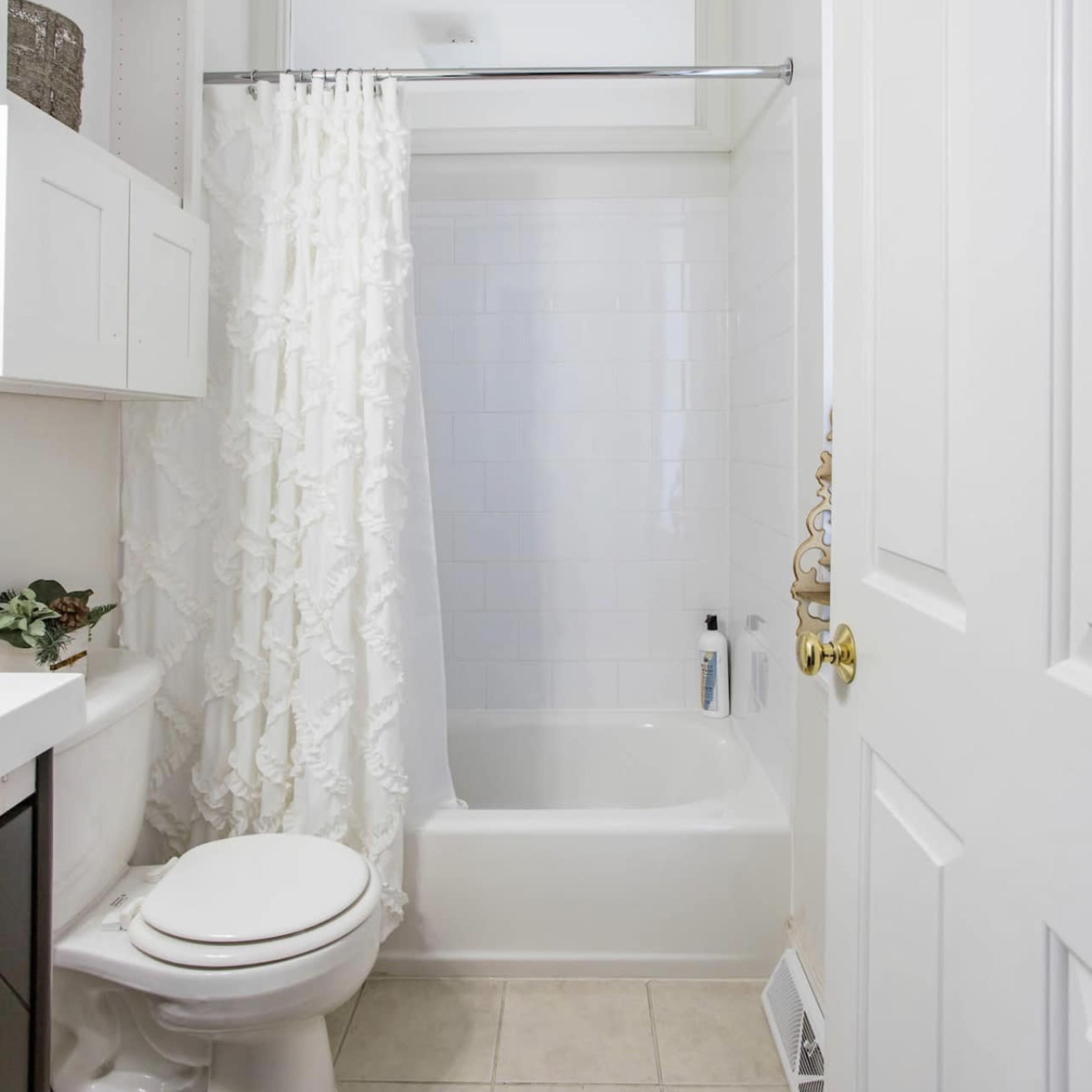 A small bathroom featuring a bathtub with a shower curtain, a toilet, and a sink with storage above.