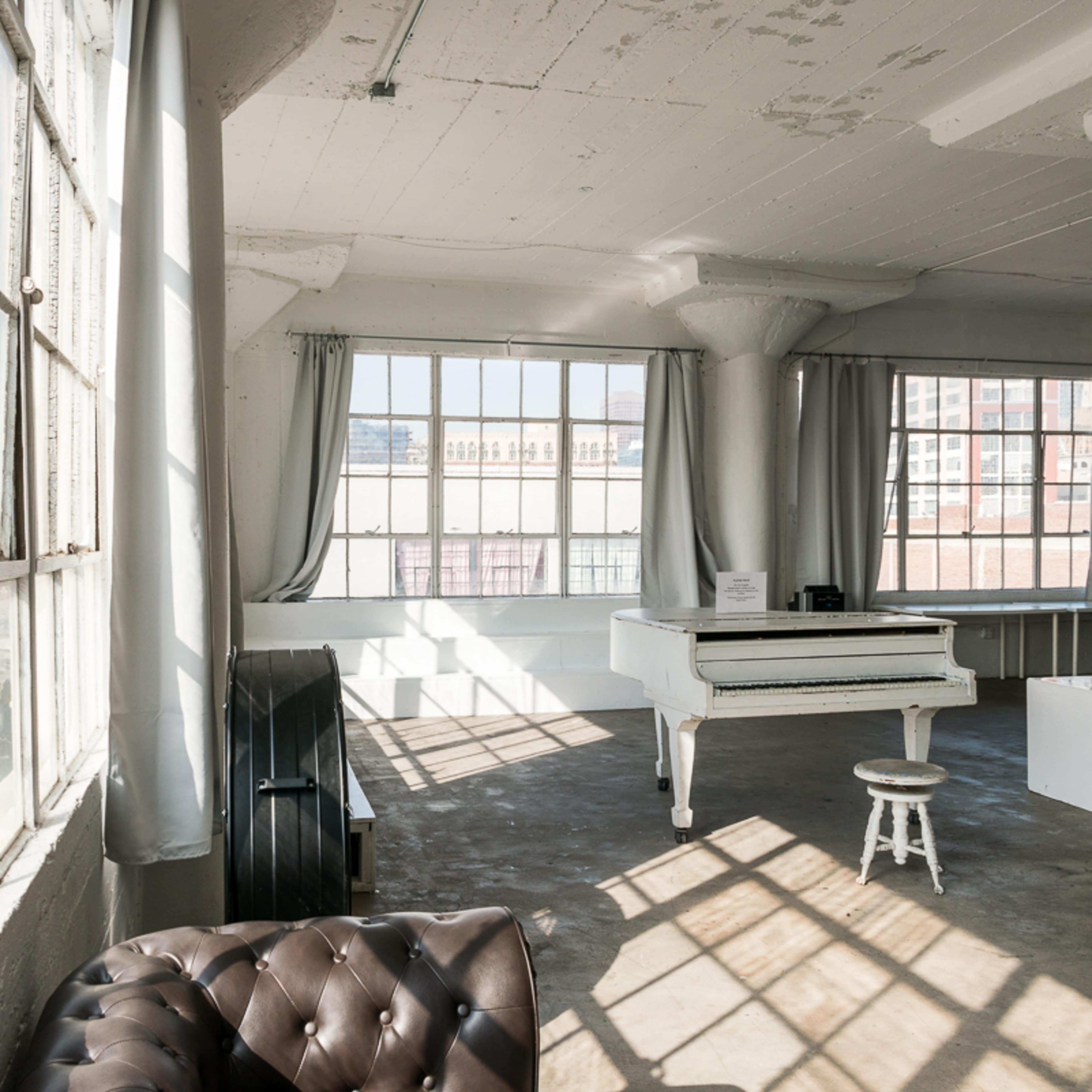 A spacious room with large windows, a white piano, and minimalist decor.