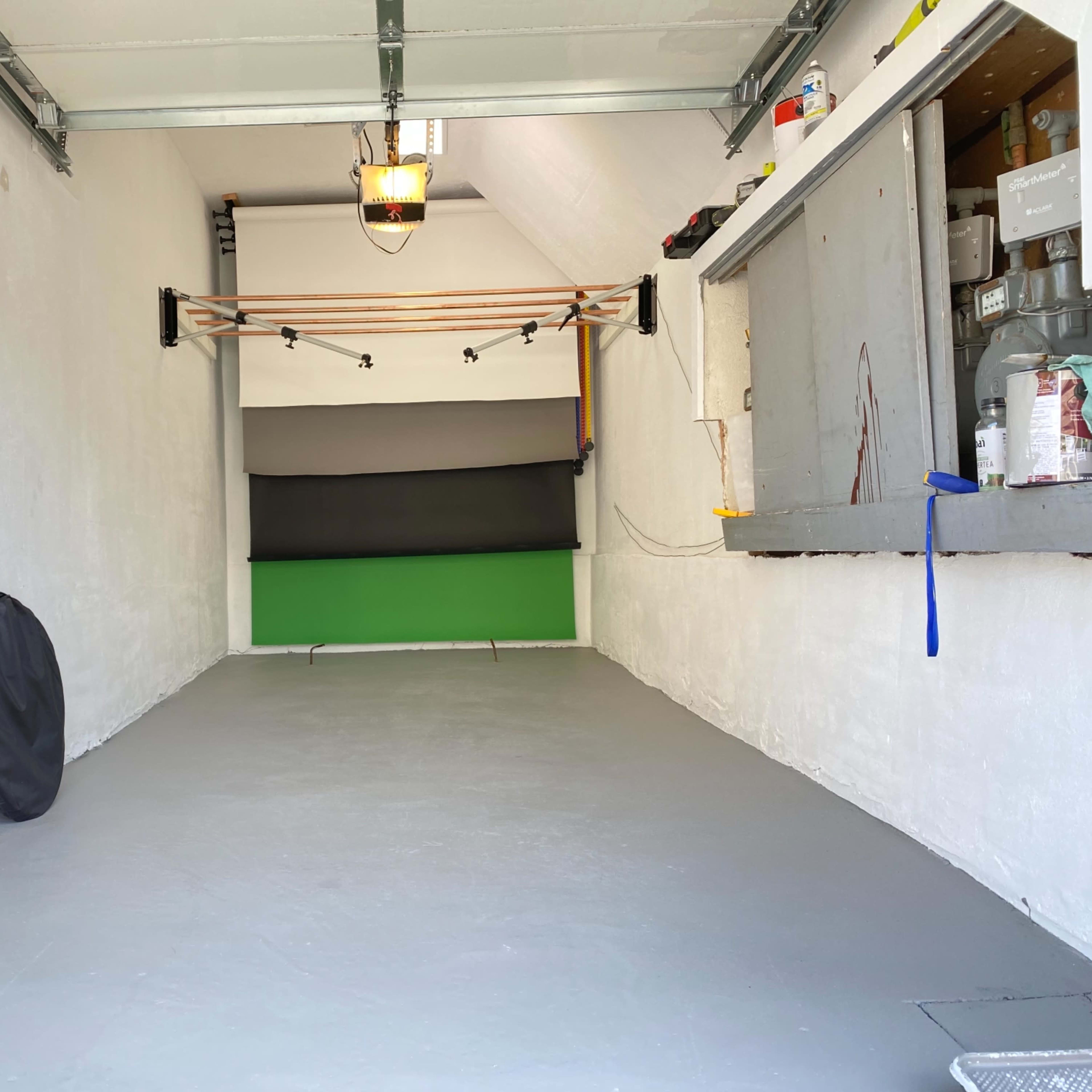 An empty garage with white walls, a gray floor, and a green backdrop at the far end.