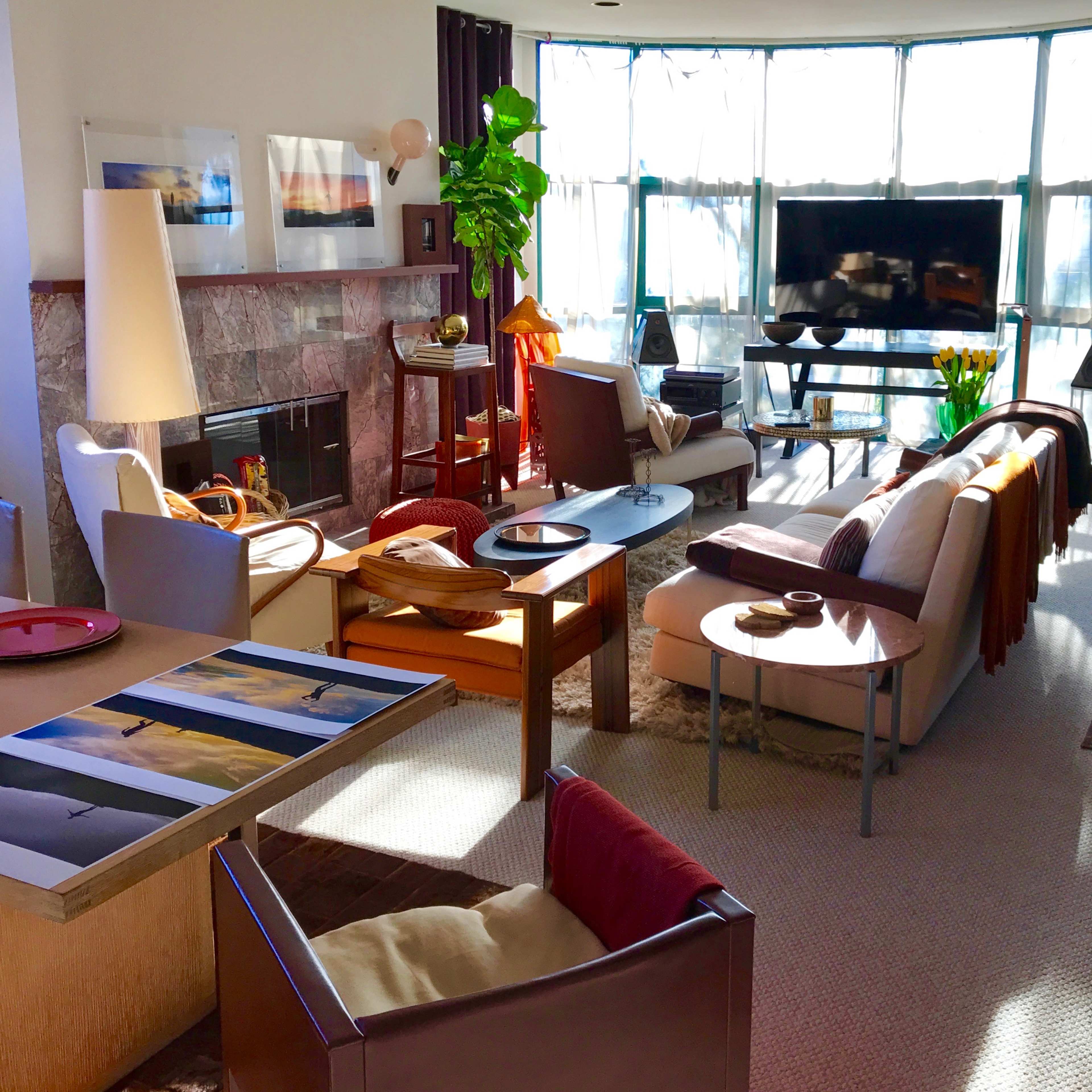 A modern living room with a fireplace, large windows, and various furniture pieces, including sofas, chairs, and a TV stand.