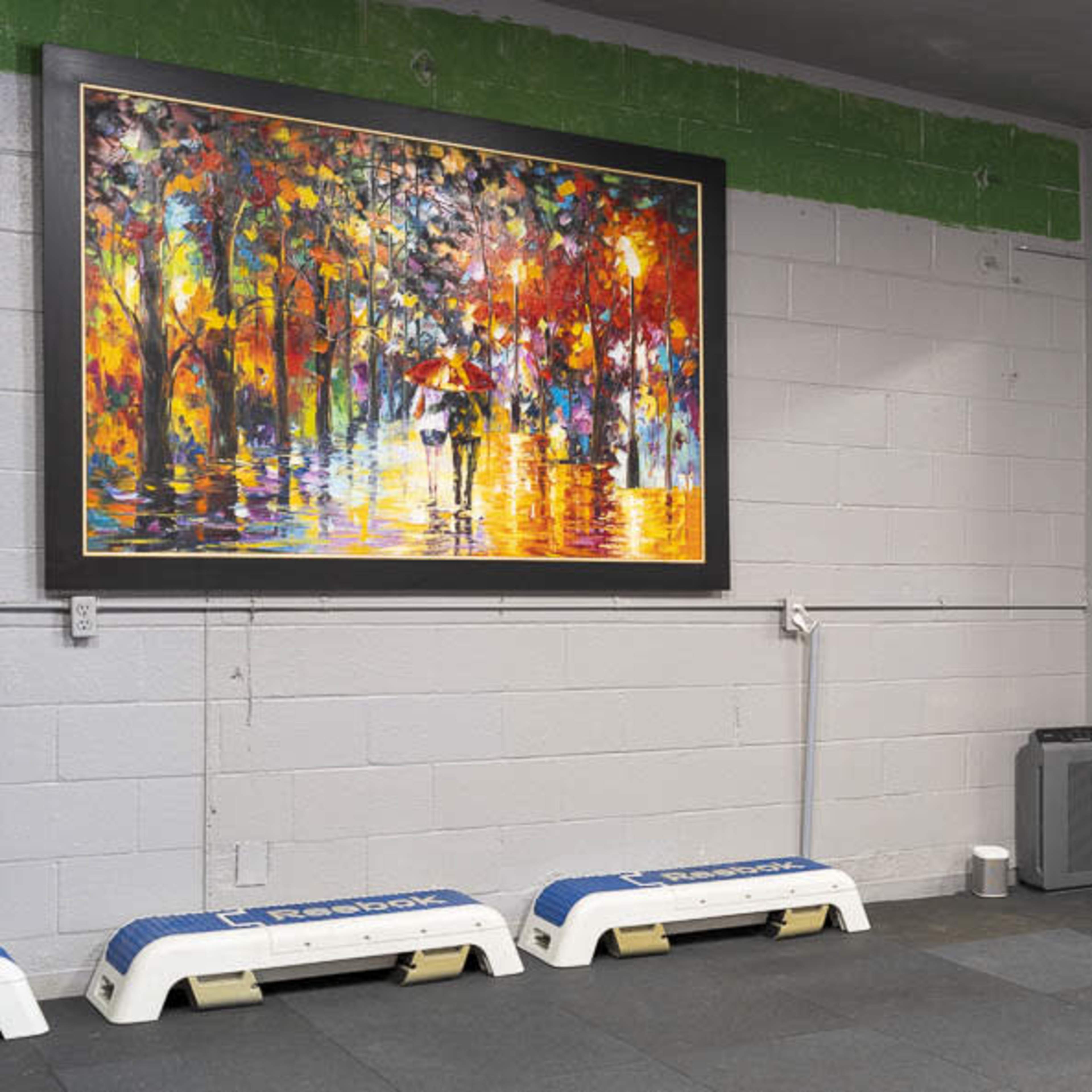 A gym area with a large colorful painting on the wall, a mirror reflecting the painting, and two white exercise benches positioned on the floor.
