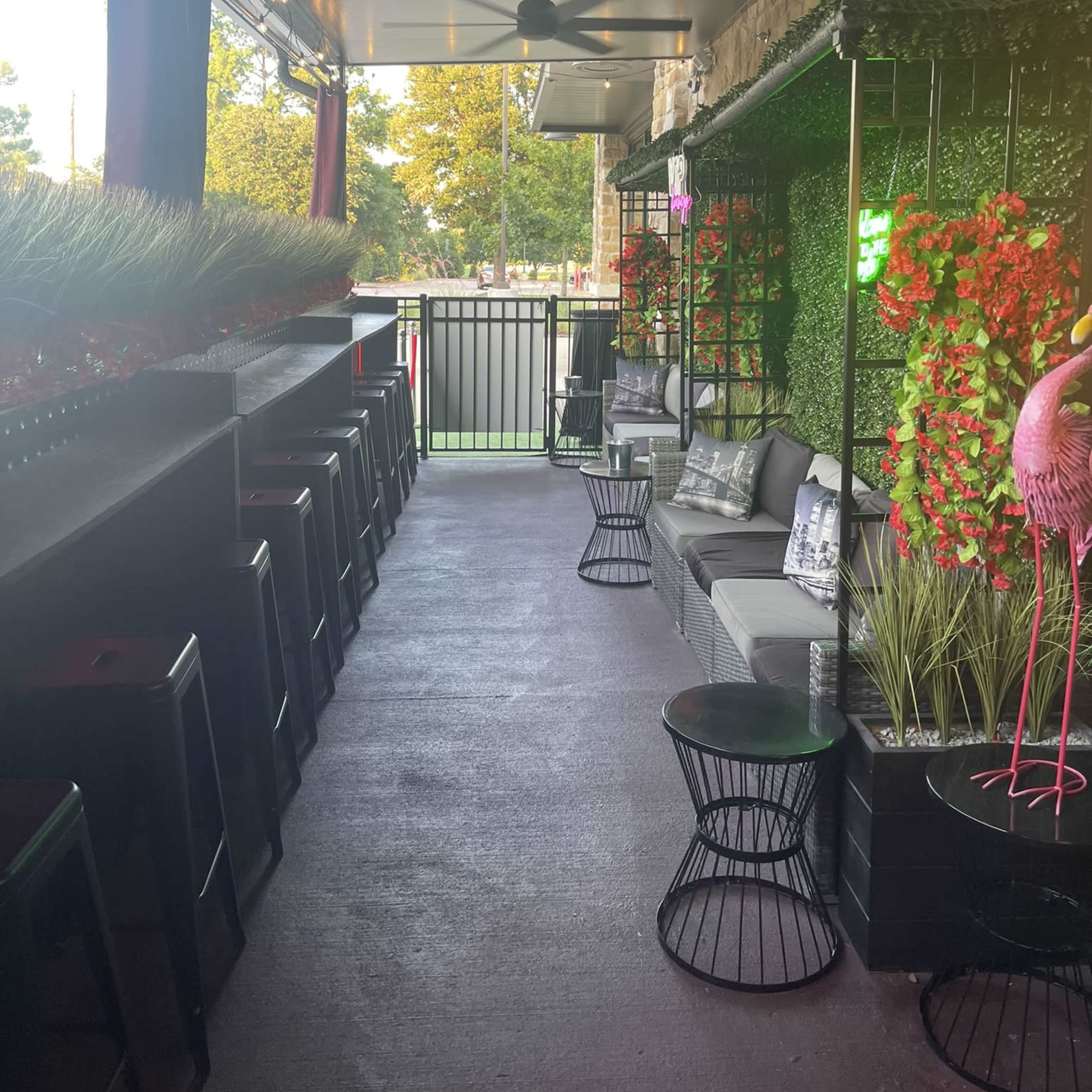 A restaurant patio area with dark seating, greenery, and decorative flowers along the walls.