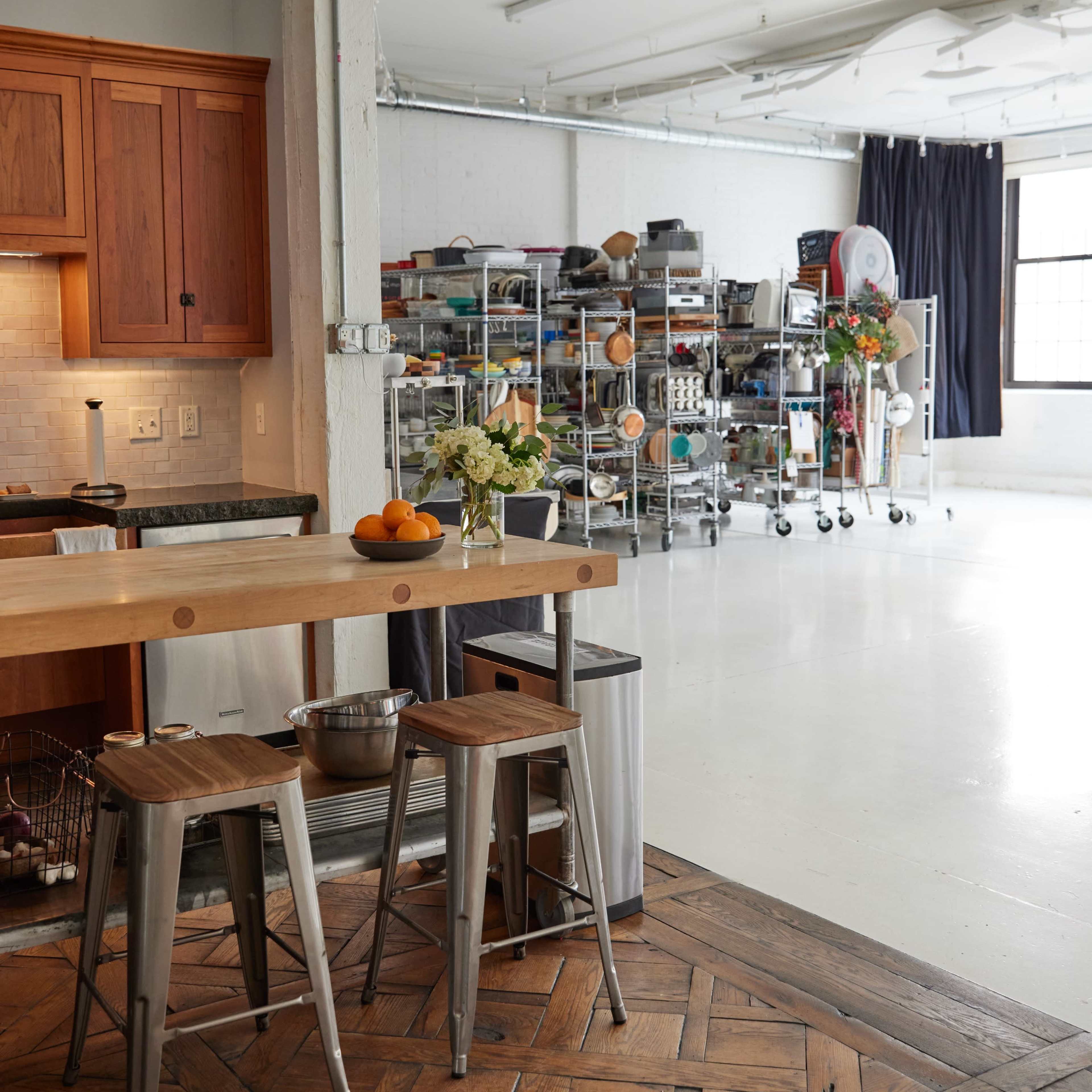 A well-organized kitchen area features wooden cabinets, metal stools, and a storage rack filled with various kitchen supplies.