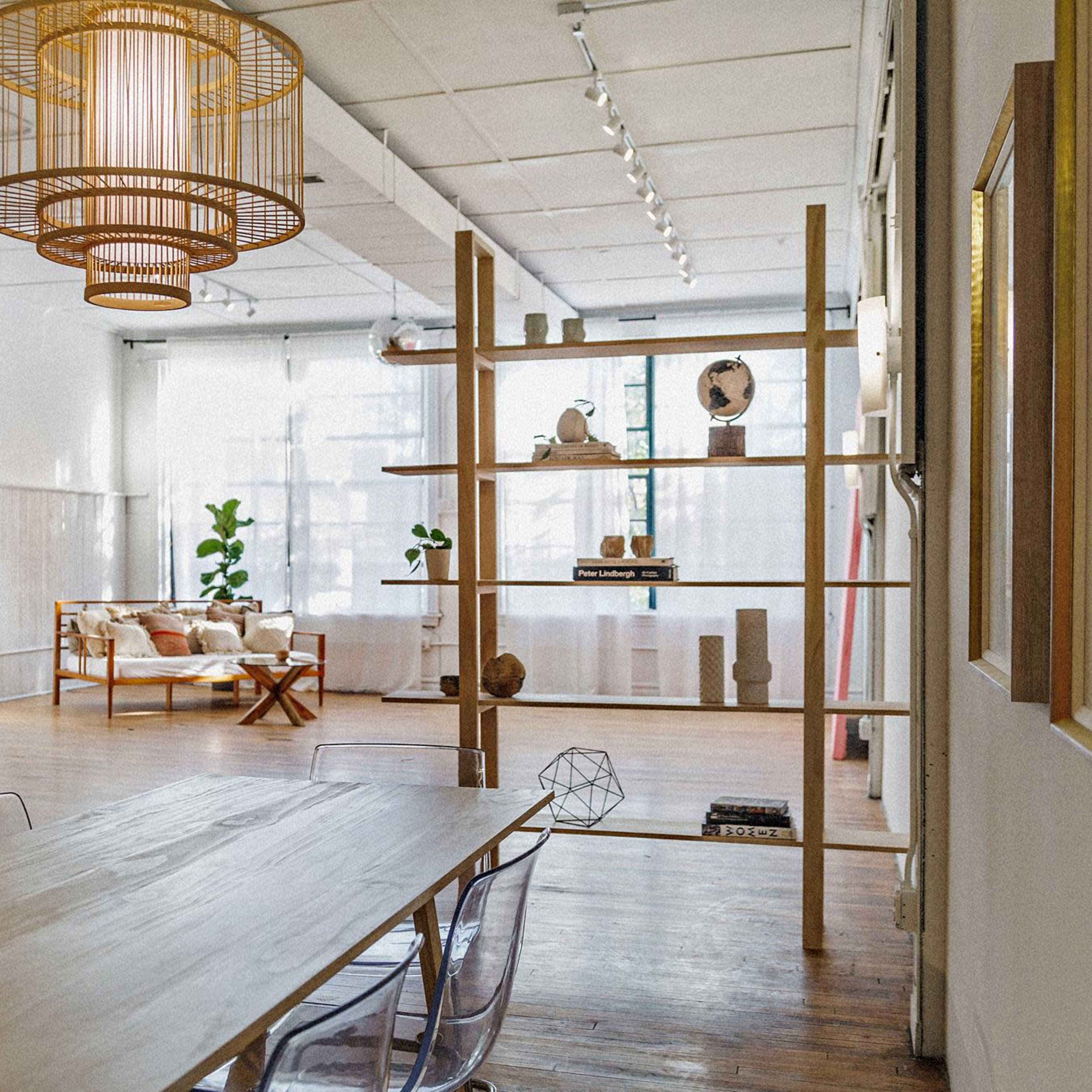 A spacious room featuring a wooden table and transparent chairs, with a shelving unit and a cozy seating area in the background.