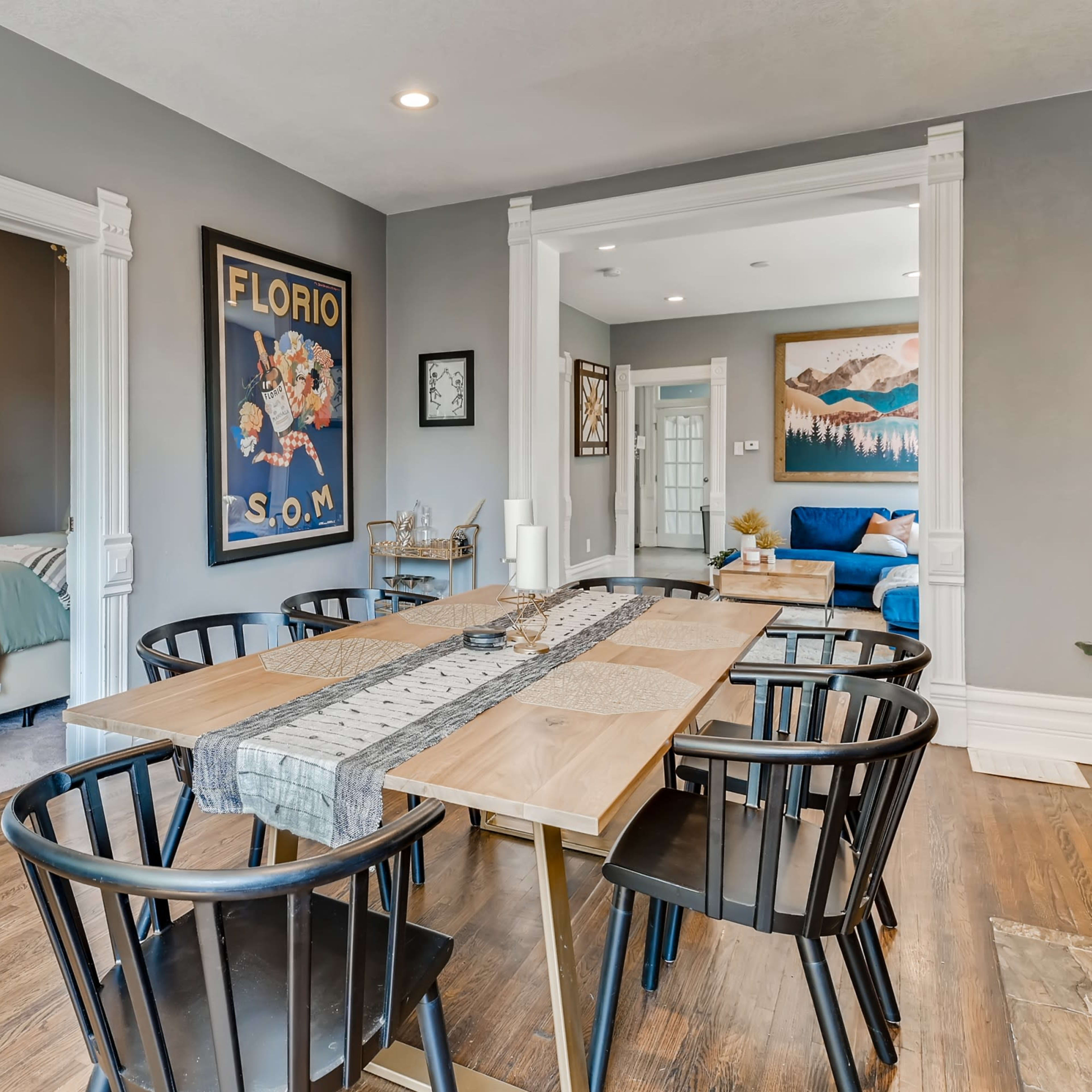A dining area with a wooden table surrounded by black chairs, featuring artwork on the walls and an adjoining living space.