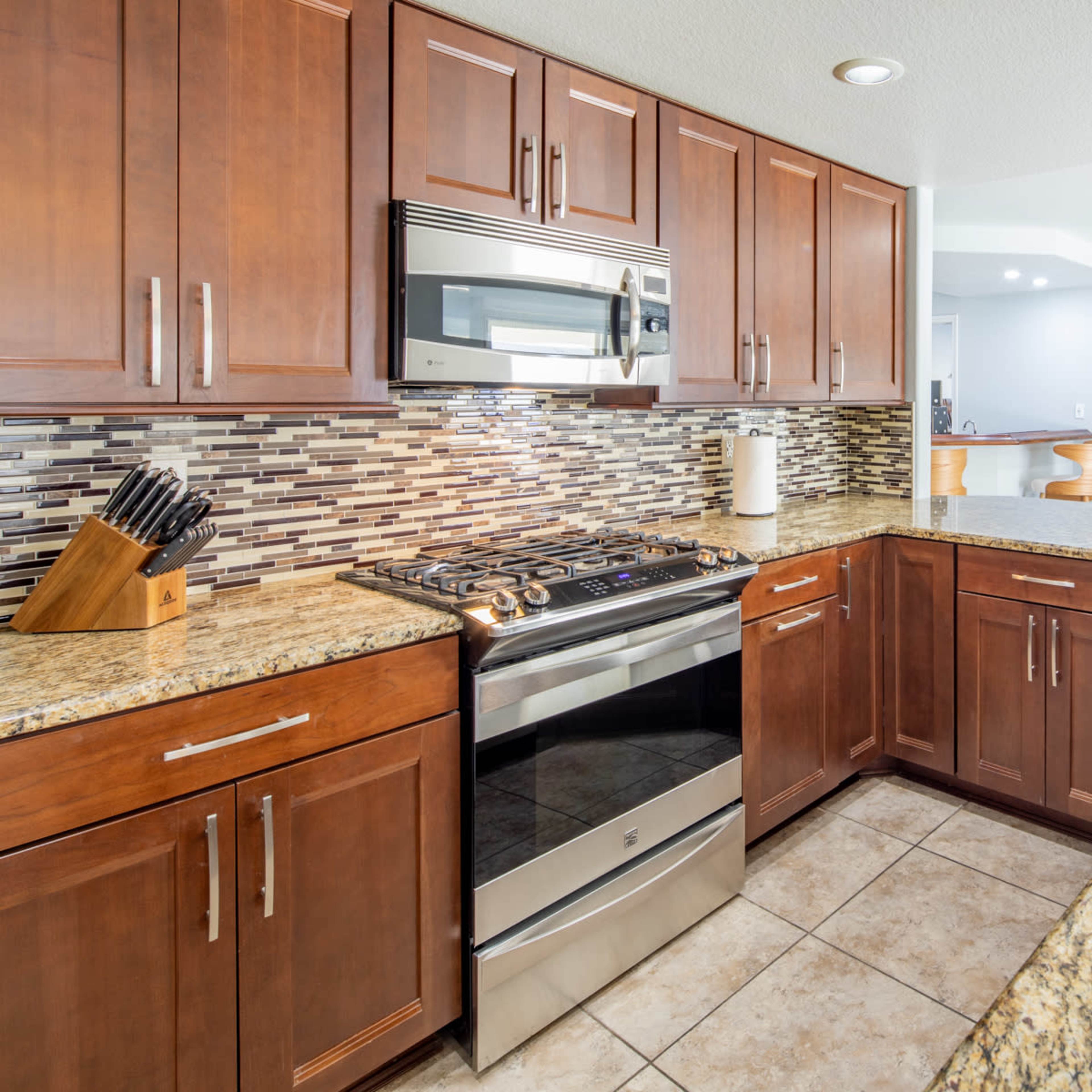 A modern kitchen with wooden cabinets, granite countertops, and stainless steel appliances, featuring a tiled backsplash and a double sink.