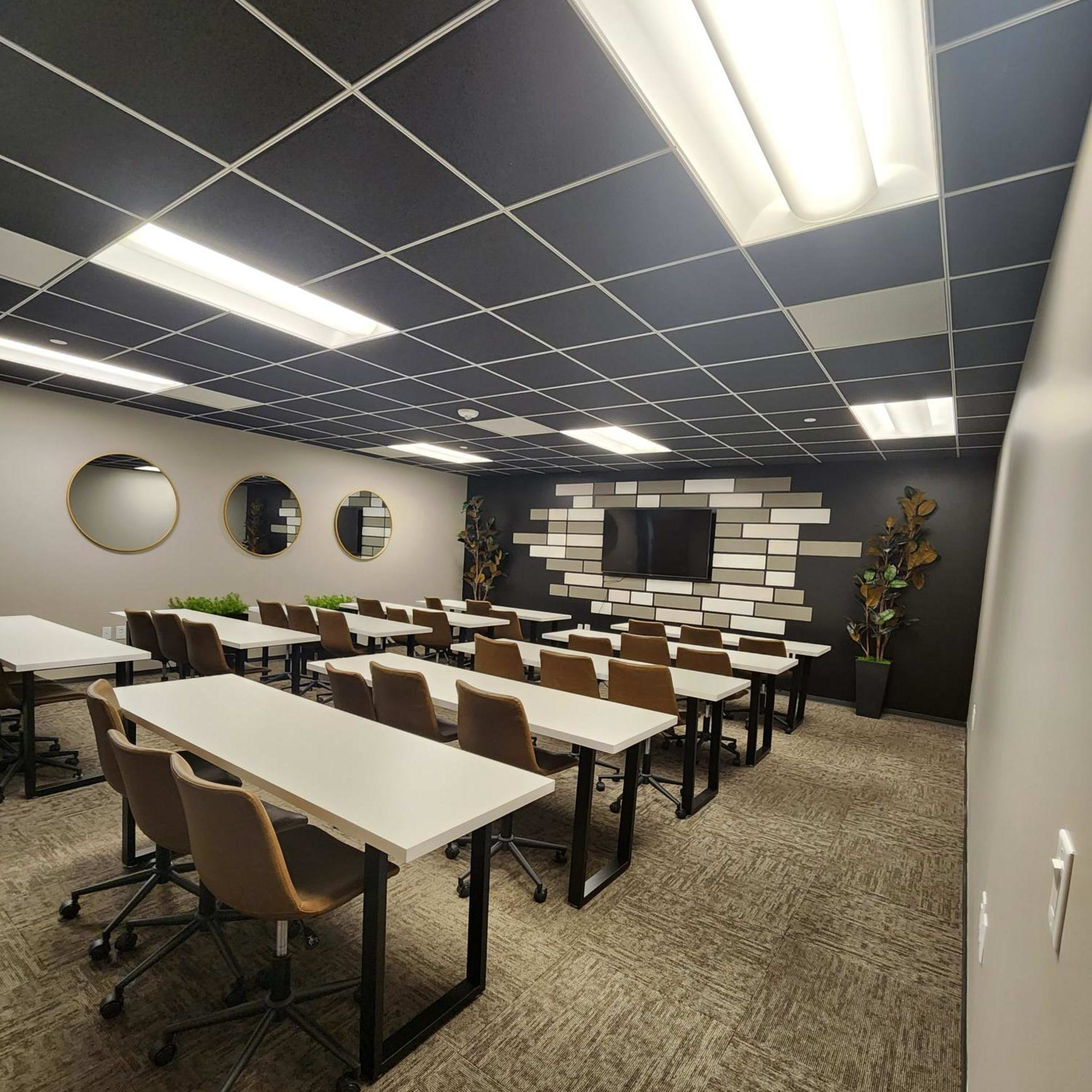 A modern classroom setup with multiple rows of white tables and brown chairs, featuring a wall mounted screen and decorative elements.