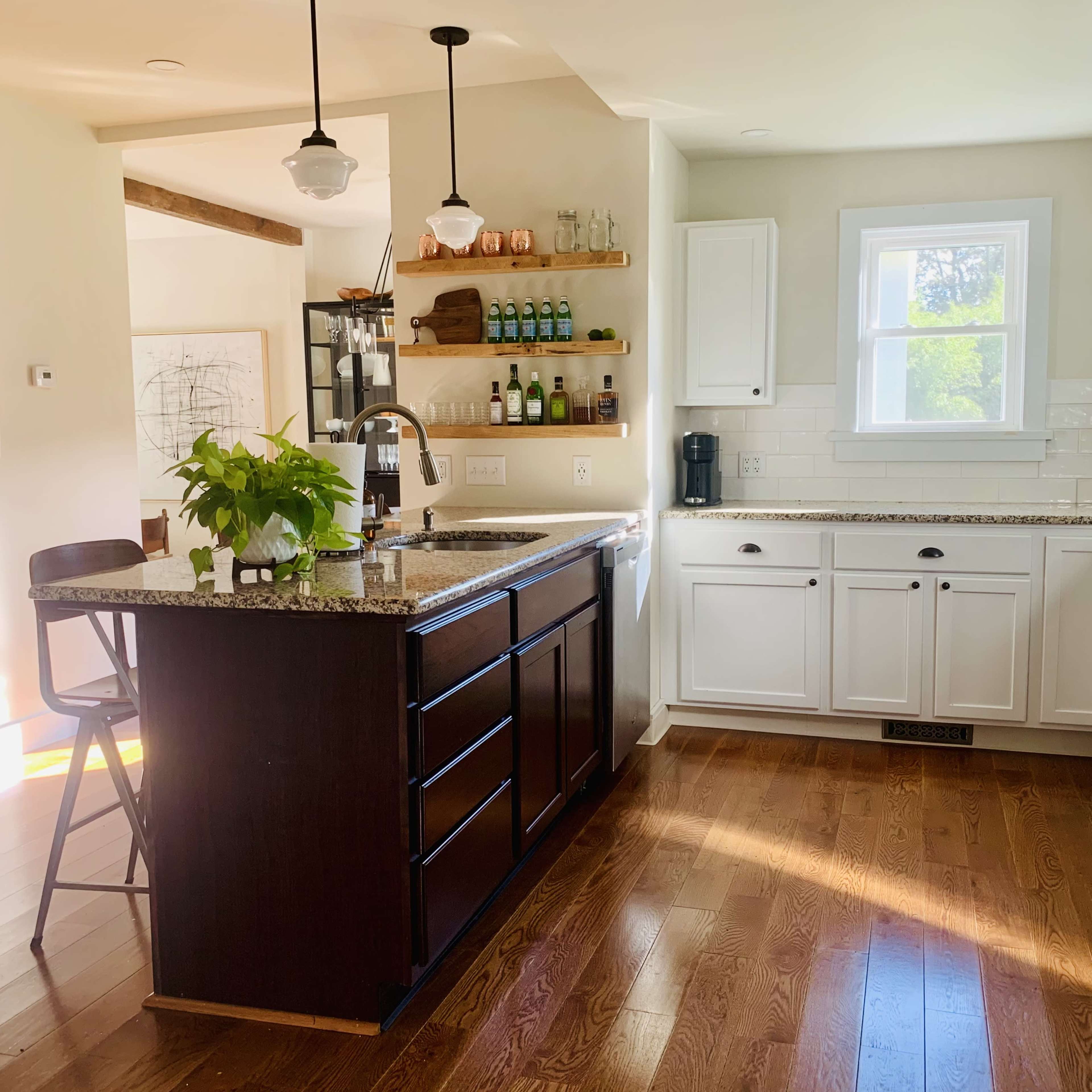A modern kitchen features white cabinetry, a granite-topped island with seating, and natural light streaming through a window.