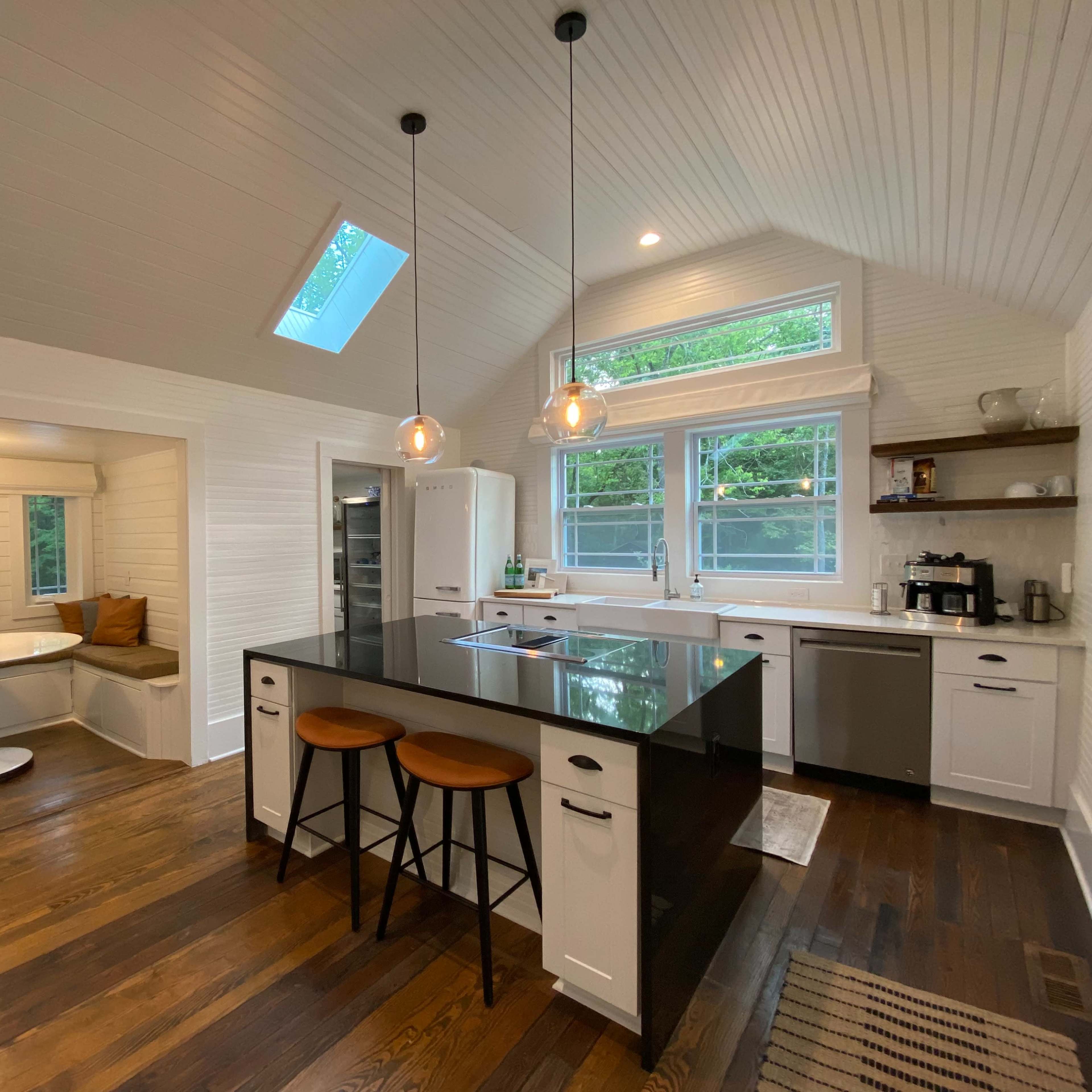 A modern kitchen with a central island, breakfast nook, and large windows letting in natural light.