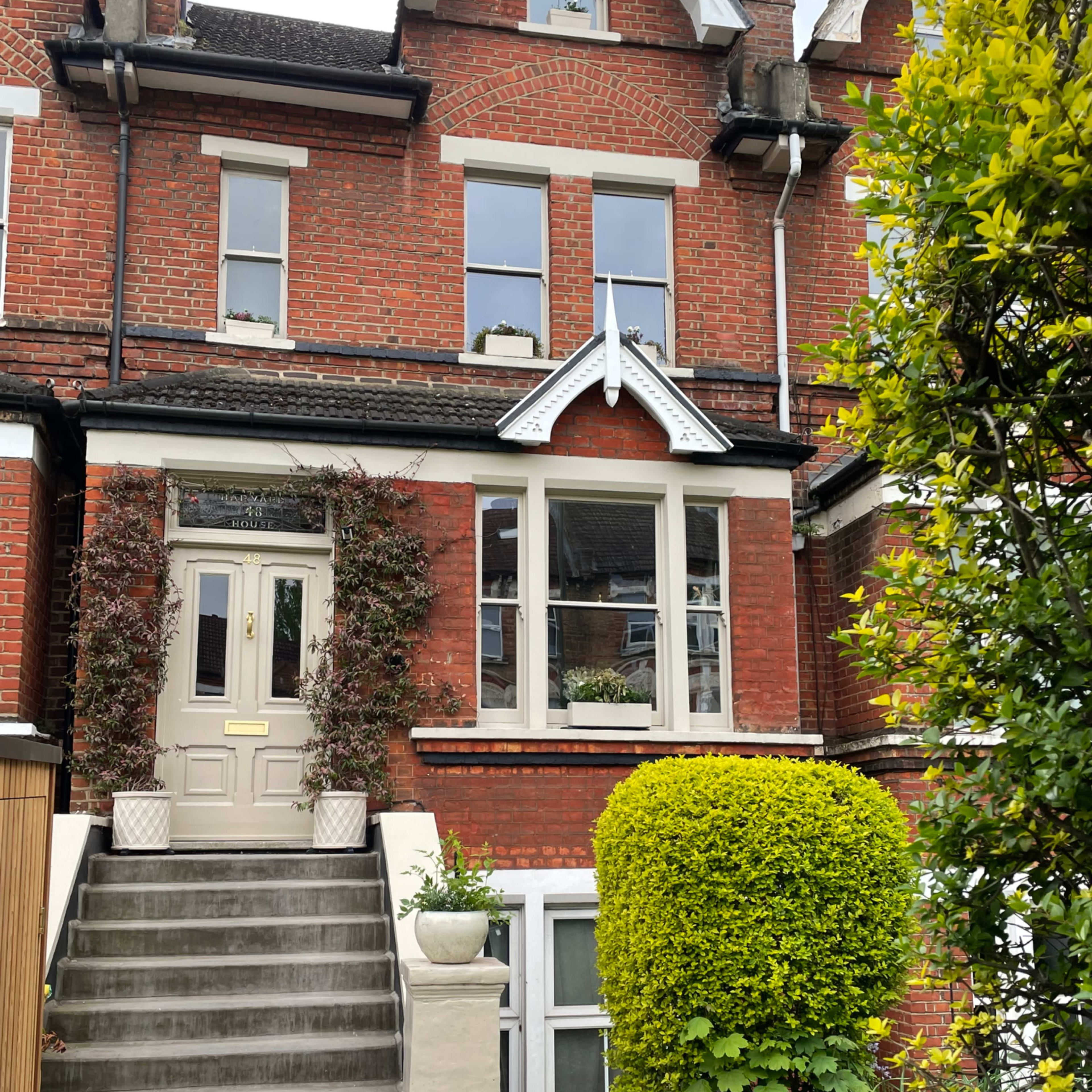 A red brick townhouse with a neatly landscaped front yard, featuring a staircase leading to the main entrance and decorative plants flanking the windows.