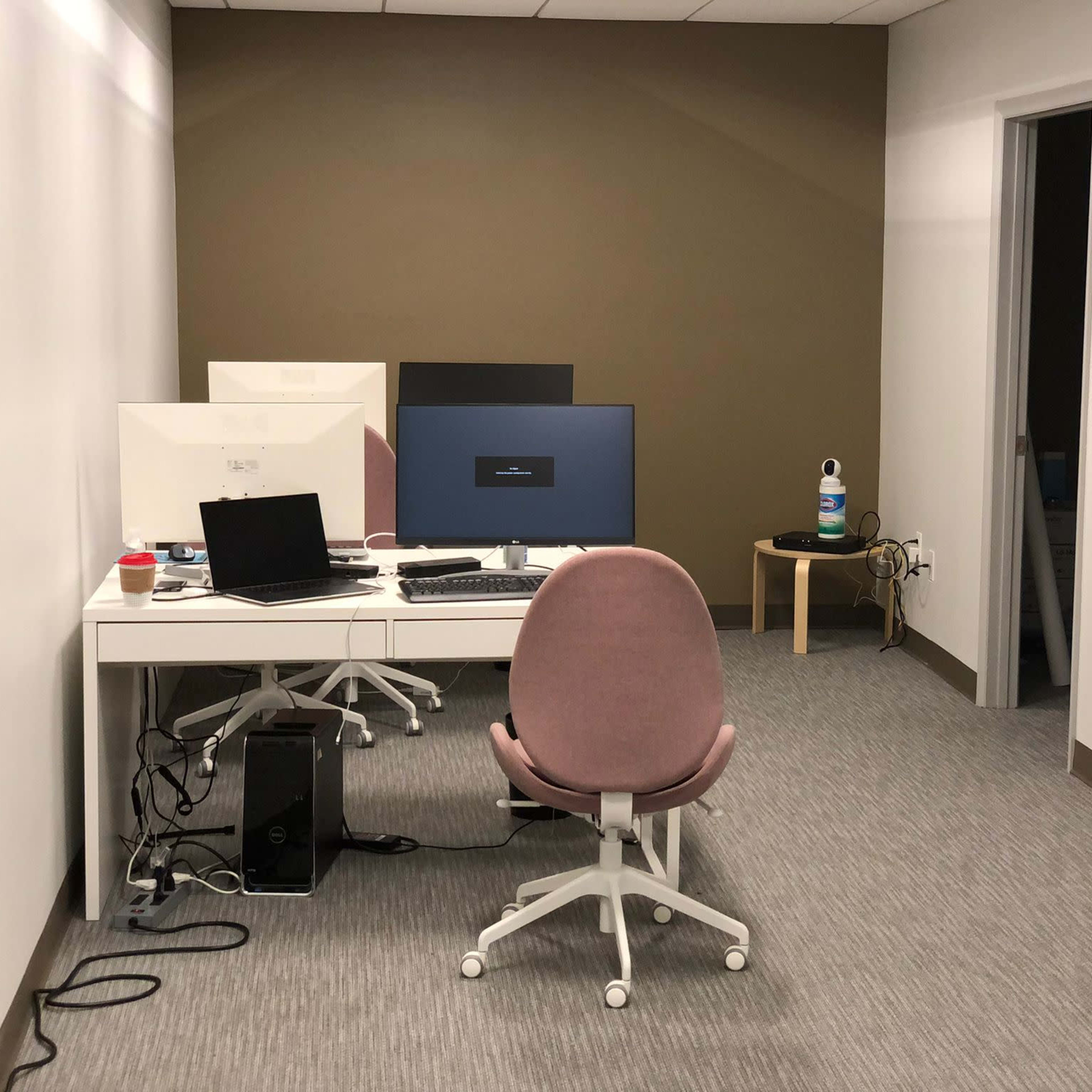 A small office space featuring a desk with three computer monitors, a chair, and a water bottle on a small table.