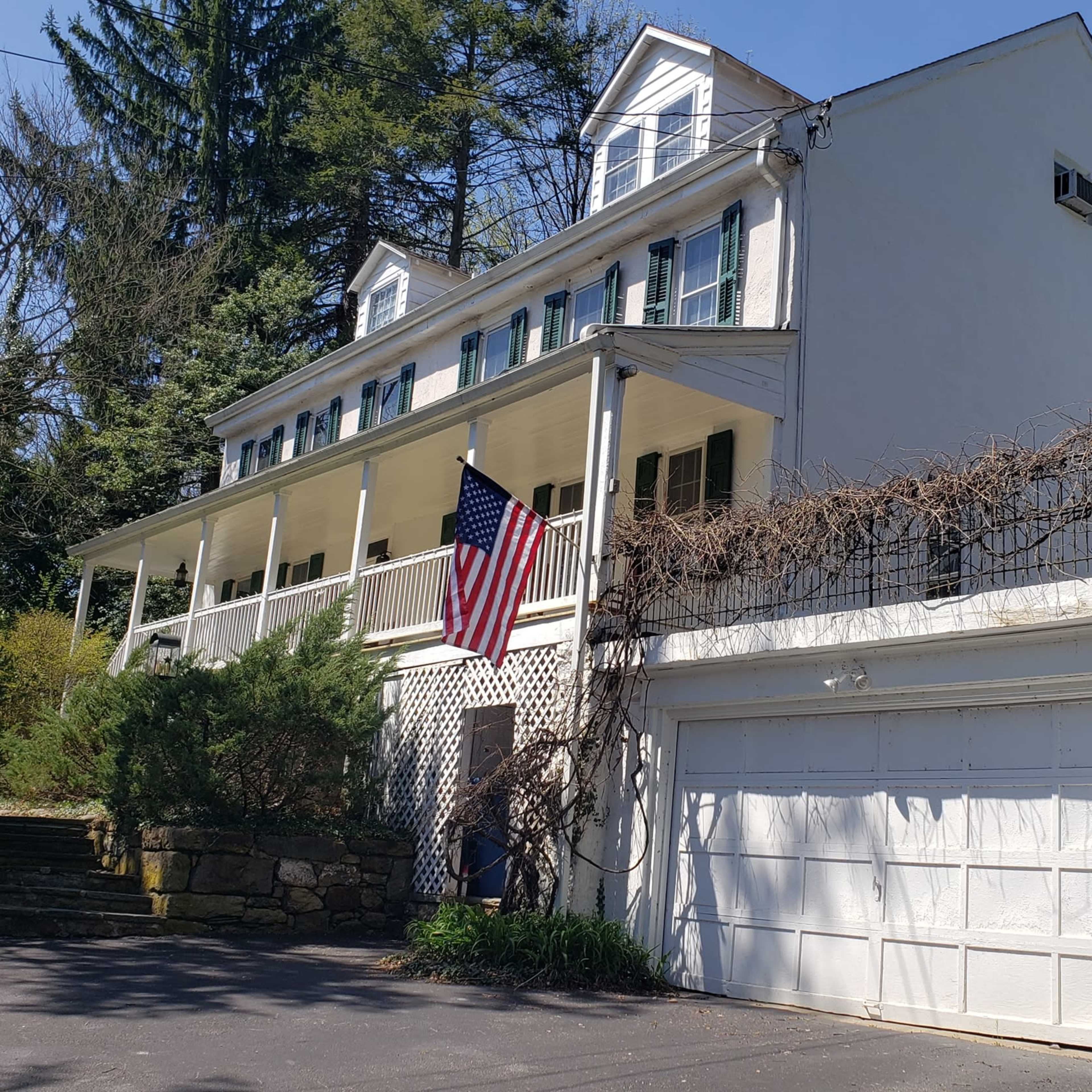 A three-story white house with a front porch, an American flag hanging, and a two-car garage.