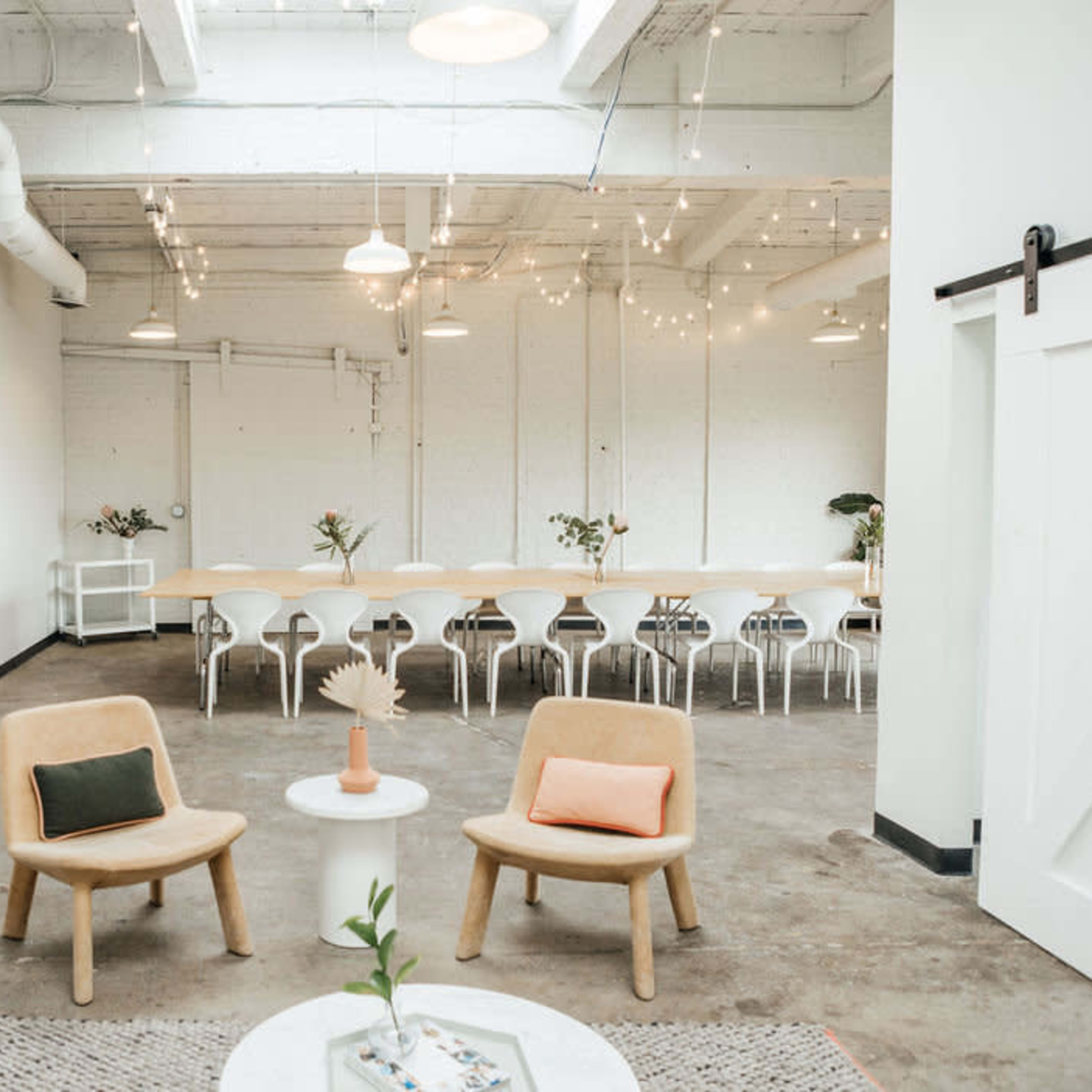 A spacious, modern interior featuring two chairs in the foreground and a long dining table with white chairs in the background.