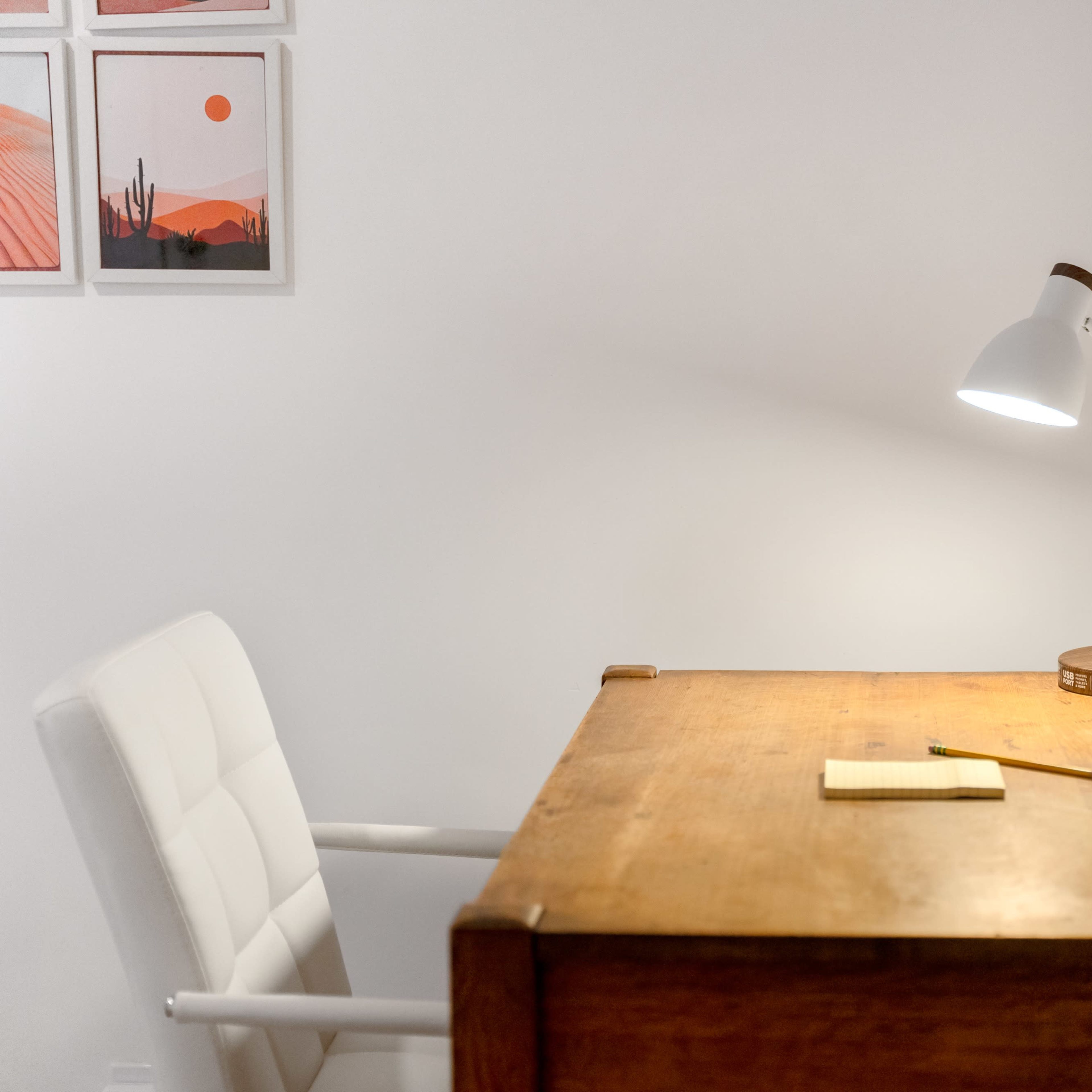 A wooden desk is positioned against a white wall, accompanied by a chair, a notepad, and a lamp providing light.