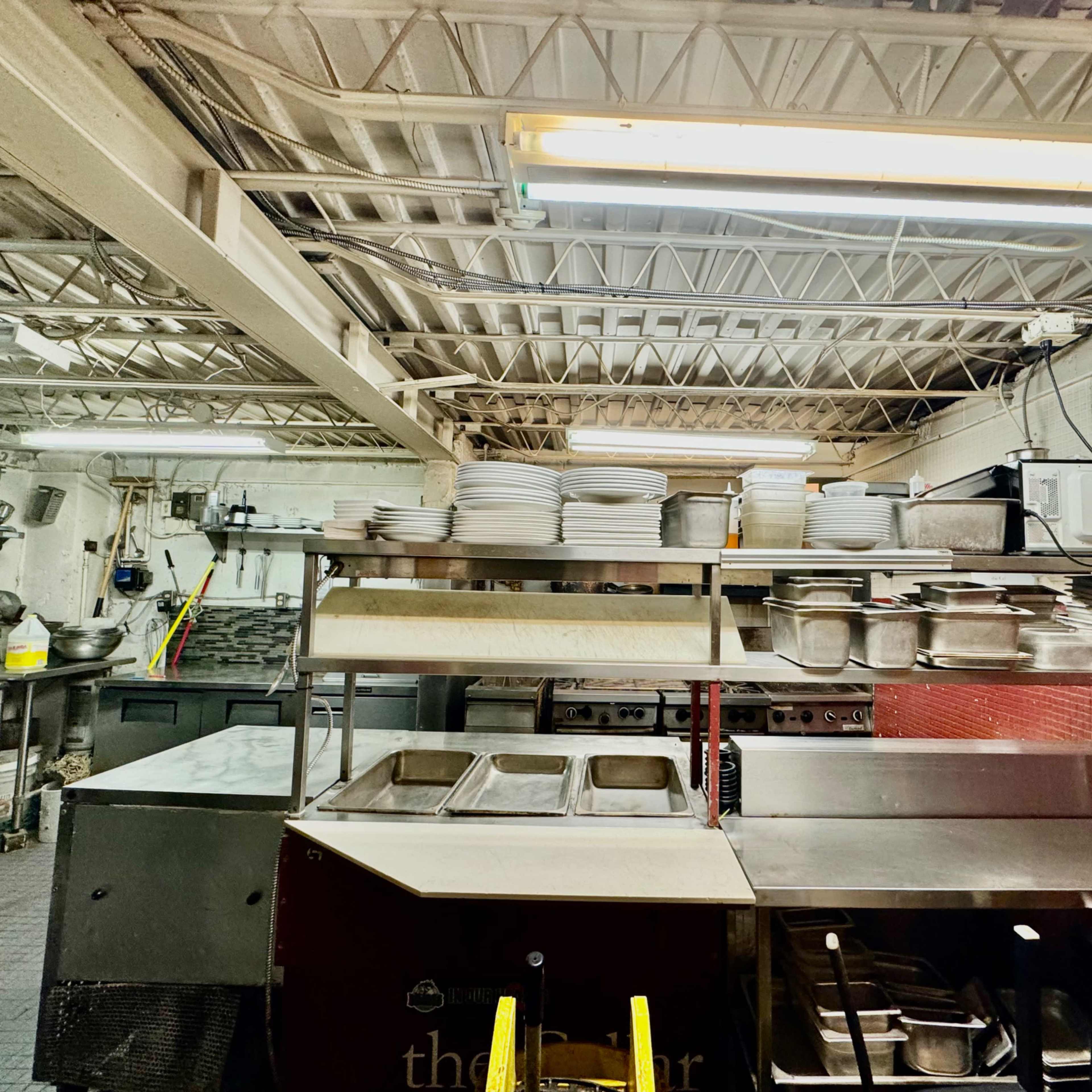 A commercial kitchen with stacked plates and various stainless steel containers arranged on shelves.