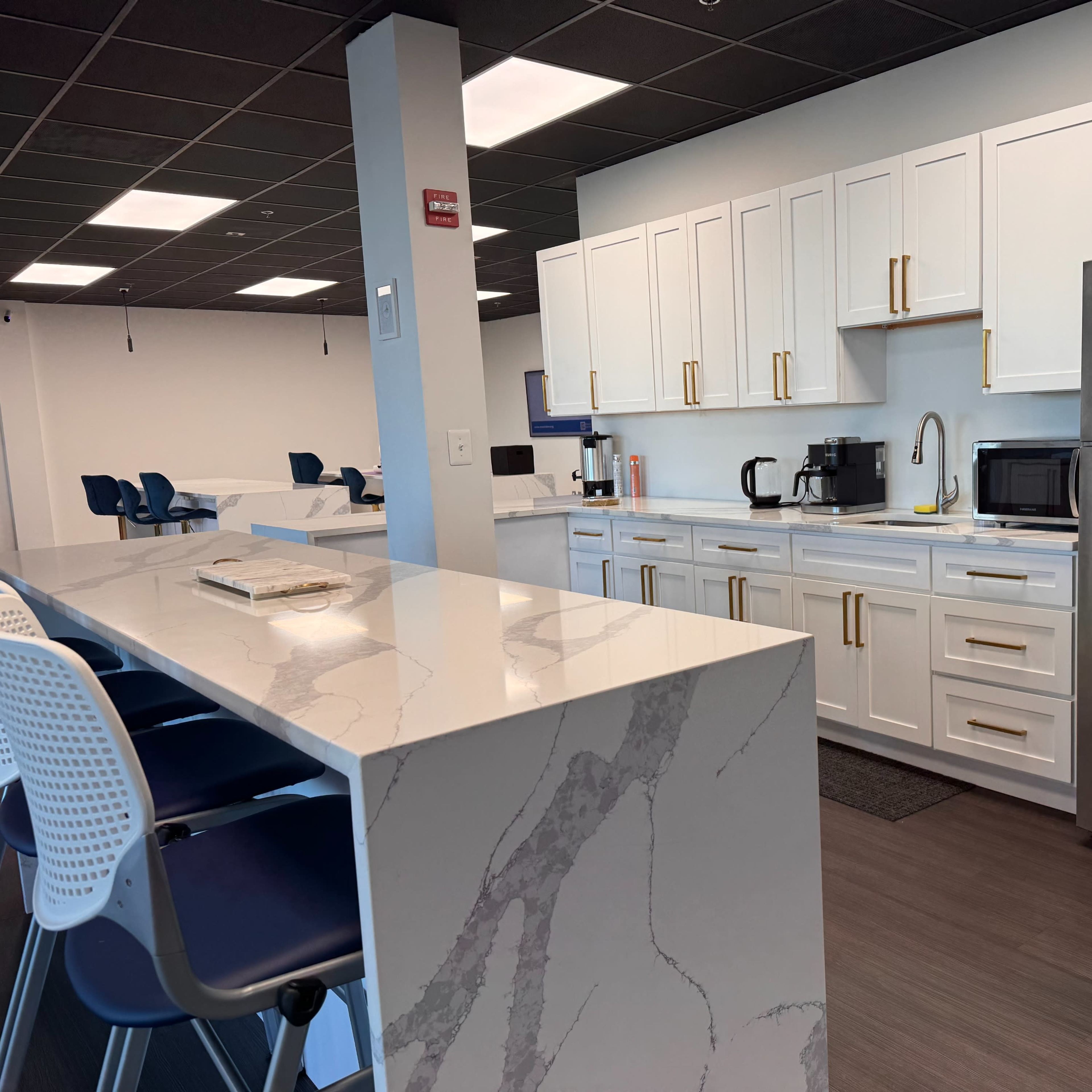 A modern kitchen area with white cabinets, stainless steel appliances, and a large marble countertop.