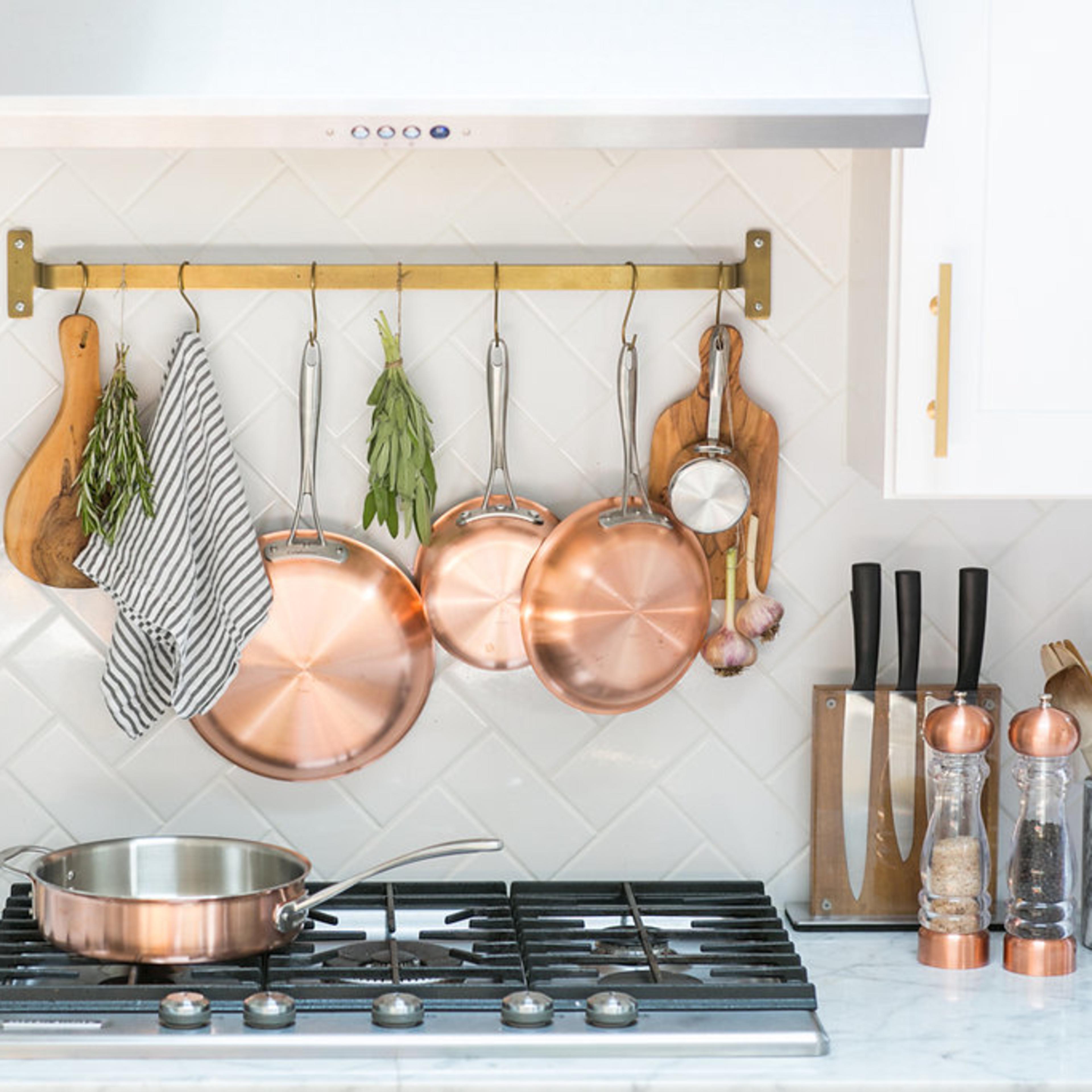 A modern kitchen with copper cookware hanging on a wall rack above a stovetop accompanied by various utensils and a spice rack.