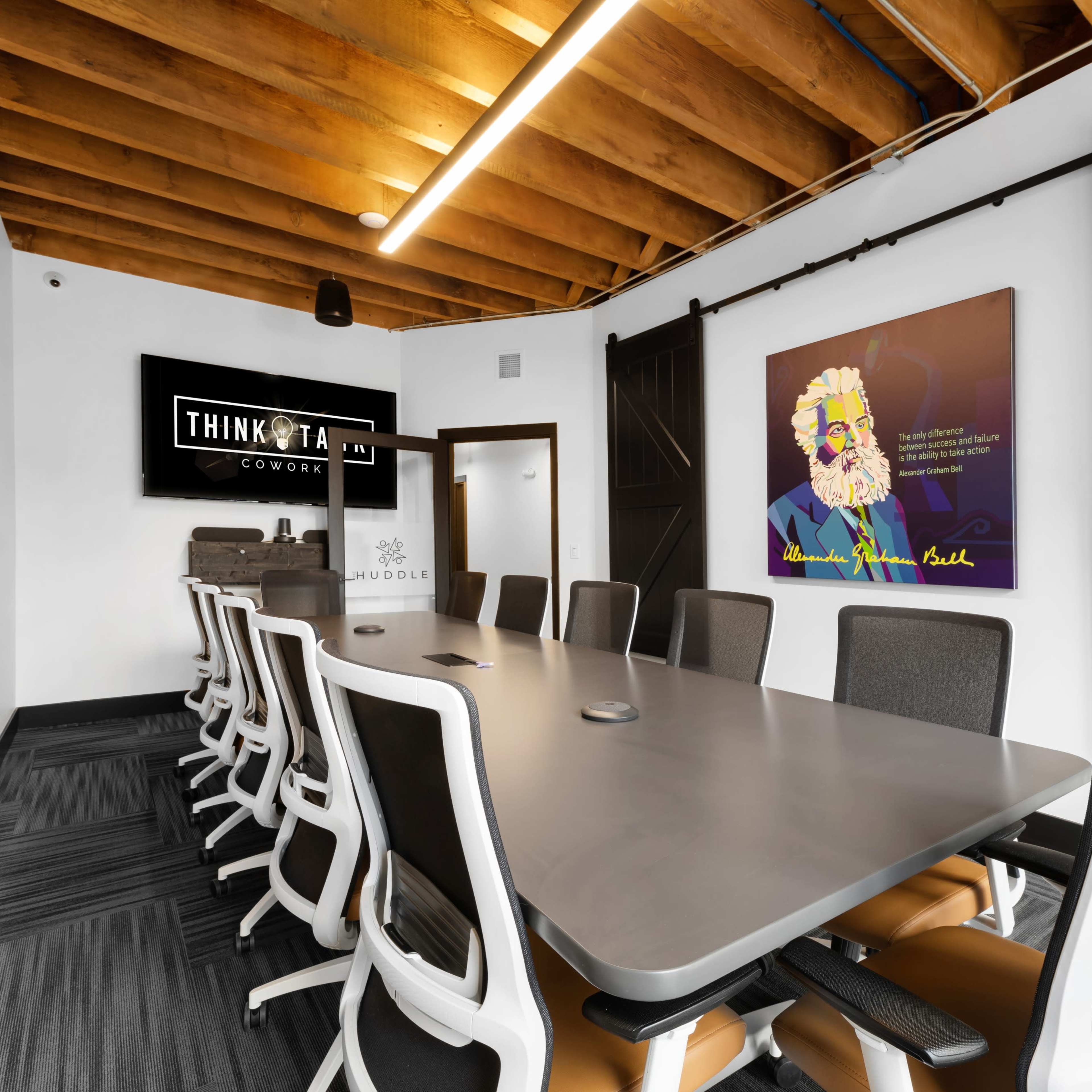 A modern conference room features a long table with ergonomic chairs, a large screen for presentations, and a colorful artwork on the wall.