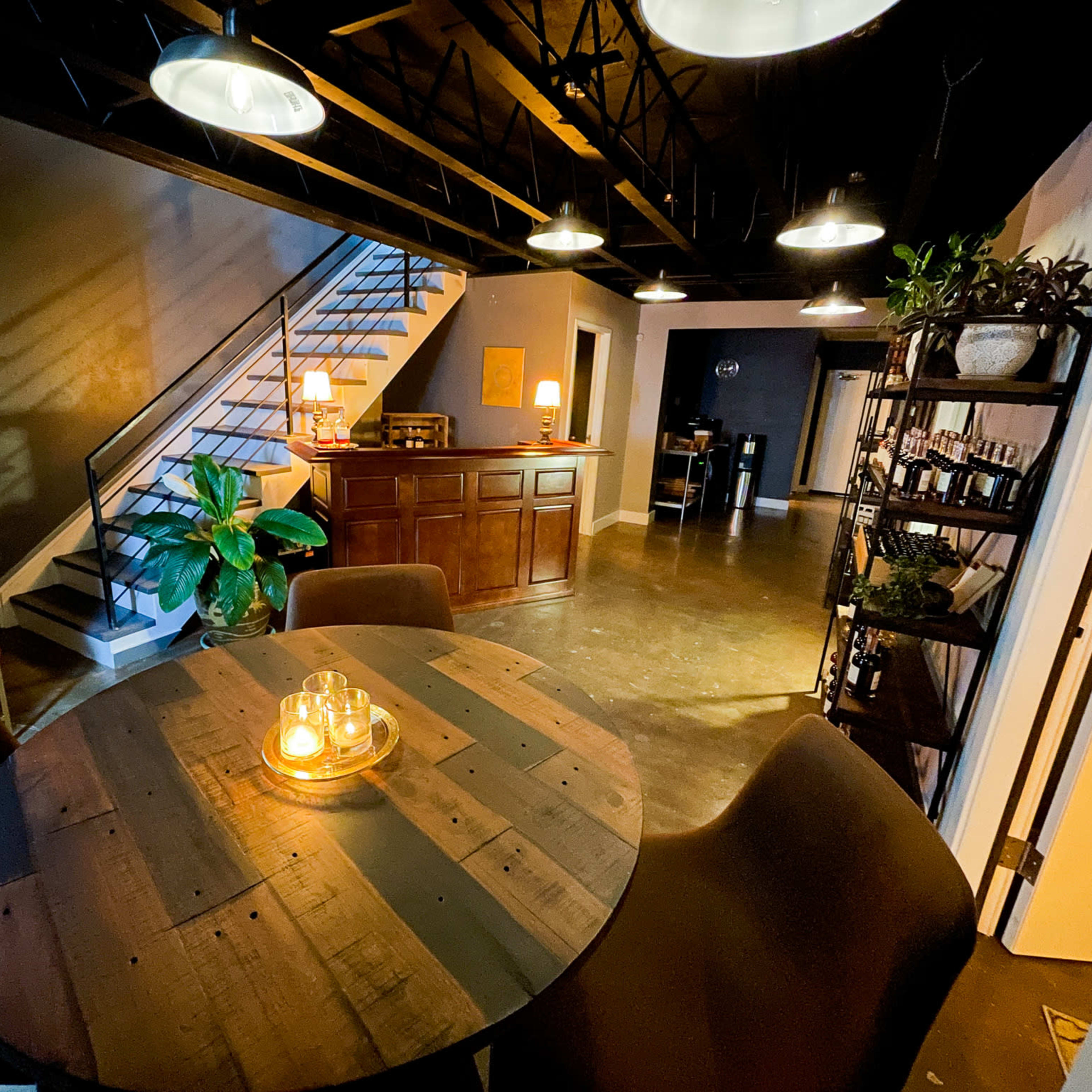 A spacious, modern interior with a round wooden table at the center, surrounded by chairs, and a staircase leading to an upper level.