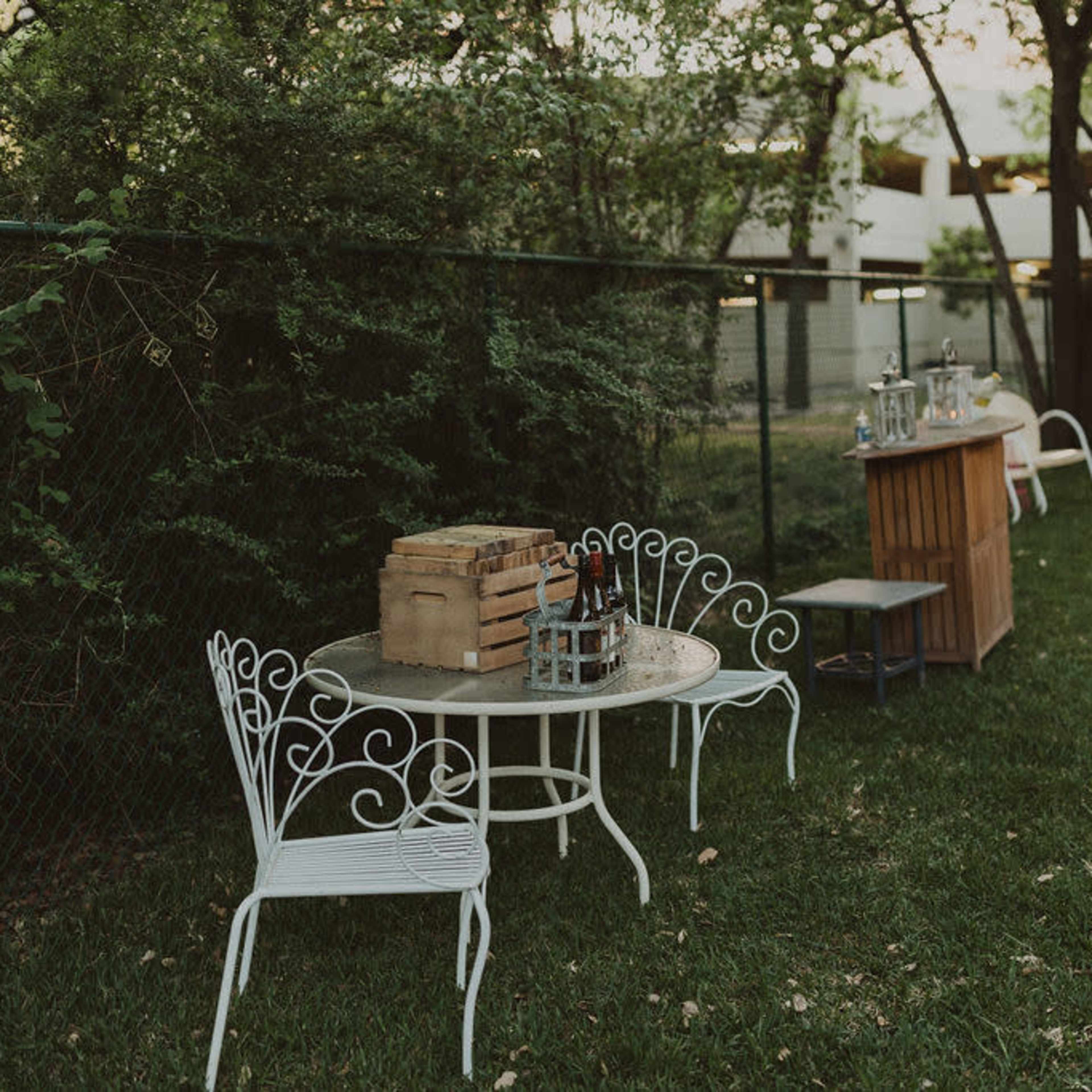 A small outdoor area features white metal furniture, a wooden crate, and various tables surrounded by greenery.